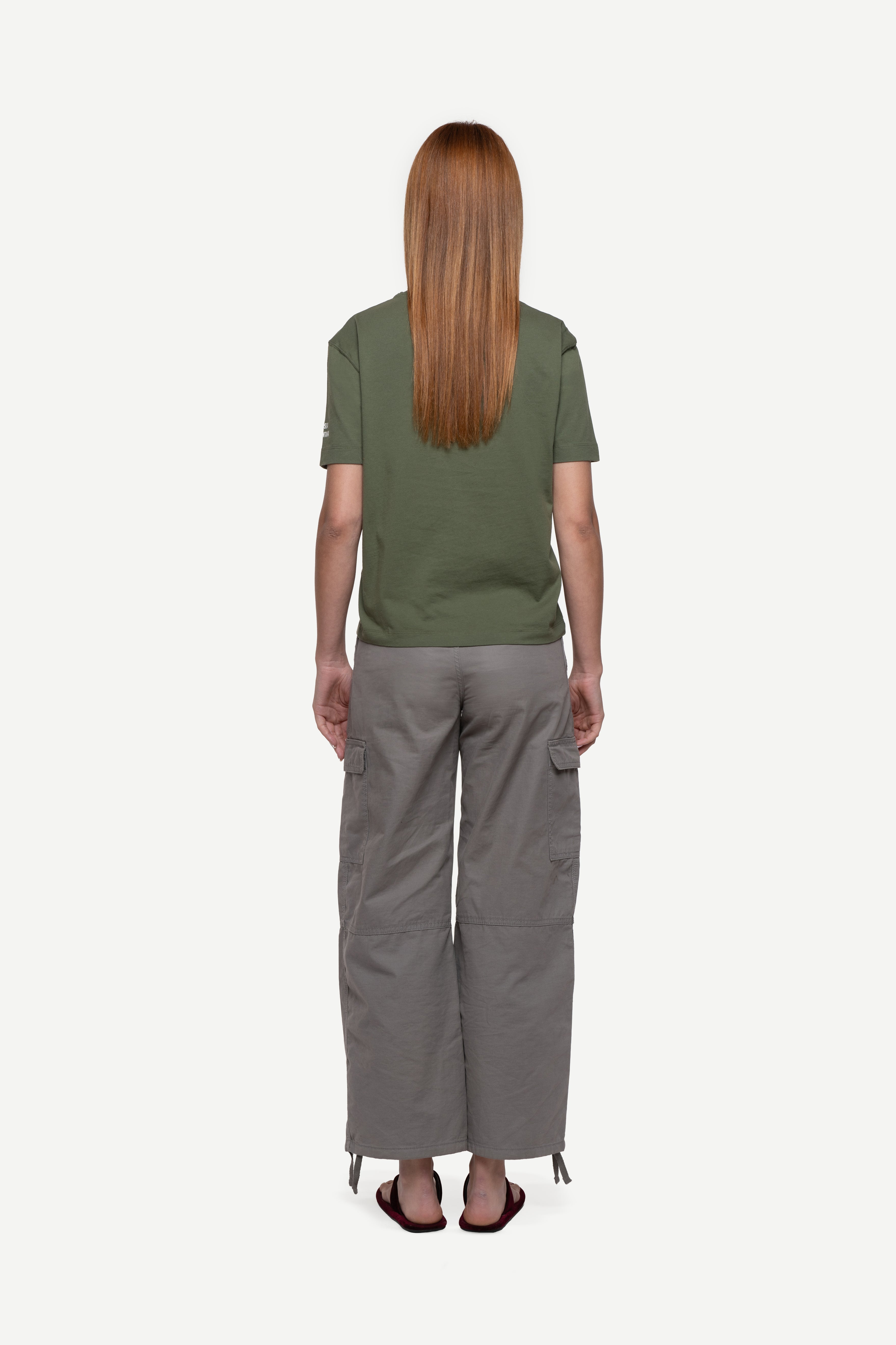 back view of woman wearing a regular fit green short-sleeved t-shirt, grey cargo pants and flip flops on a white background
