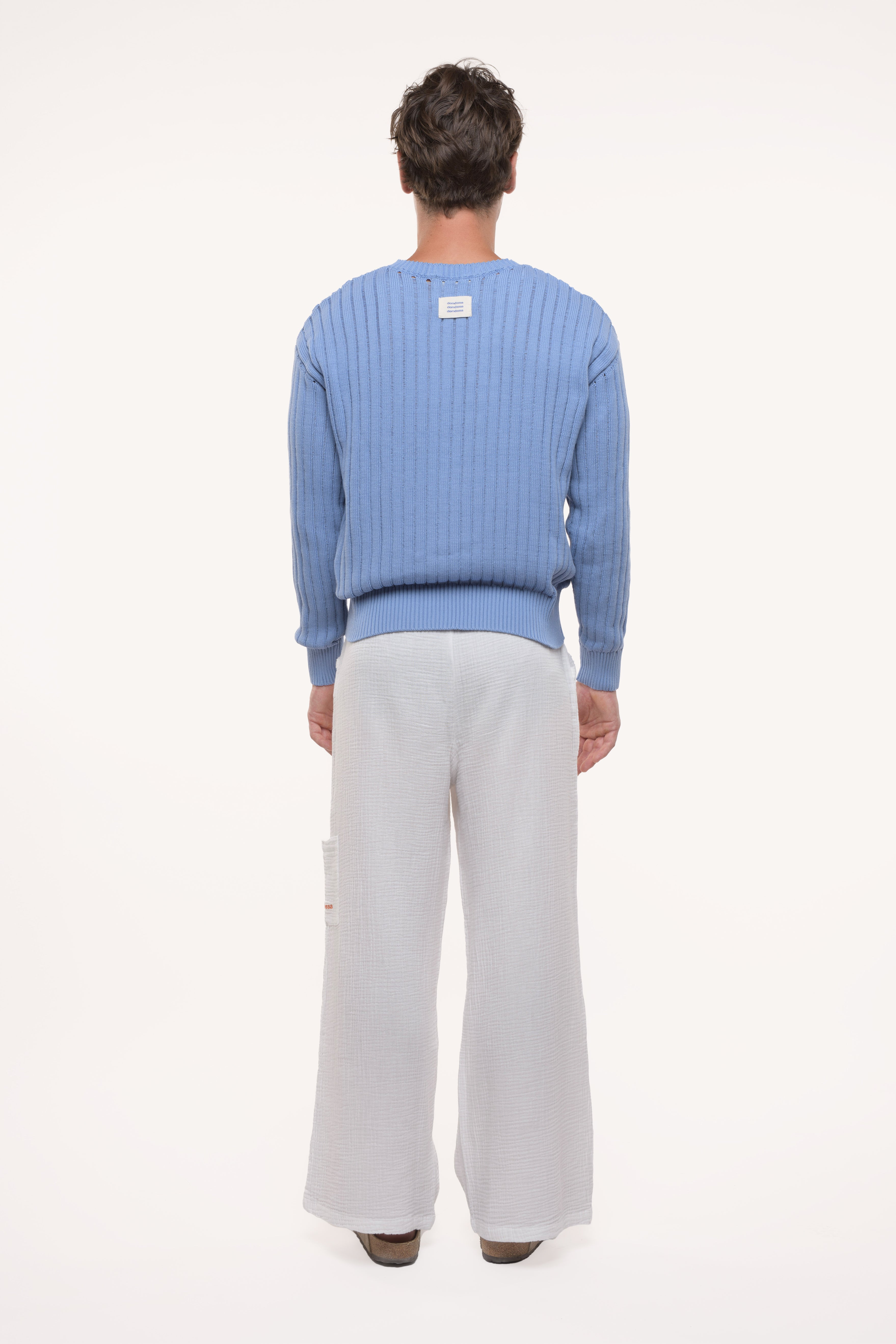 Back view of a man wearing a blue sweater and light gray pants on a white background