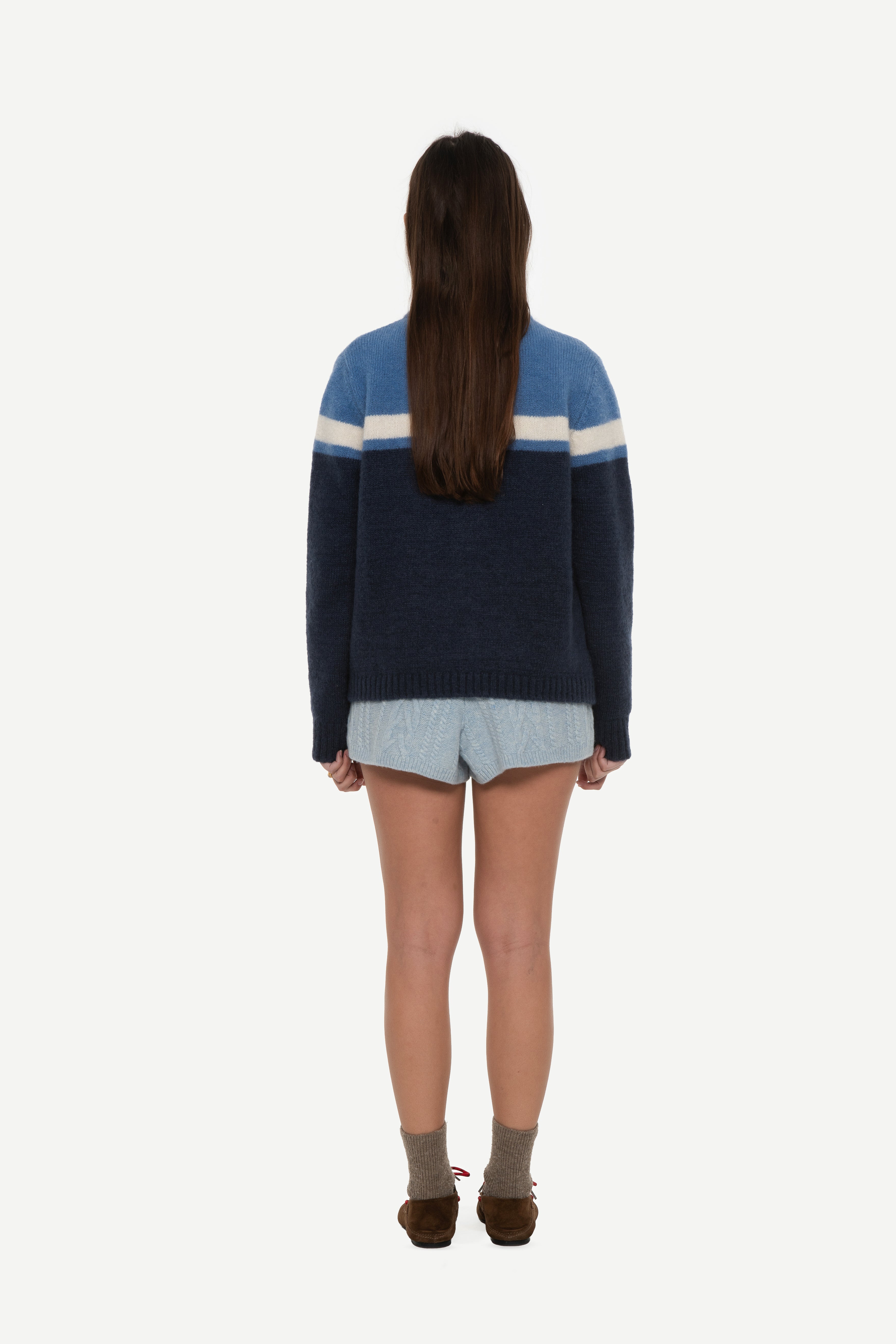 back view of woman wearing a mohair zip cardigan with two shades of blue and white stripe at chest and blue shorts on a white background