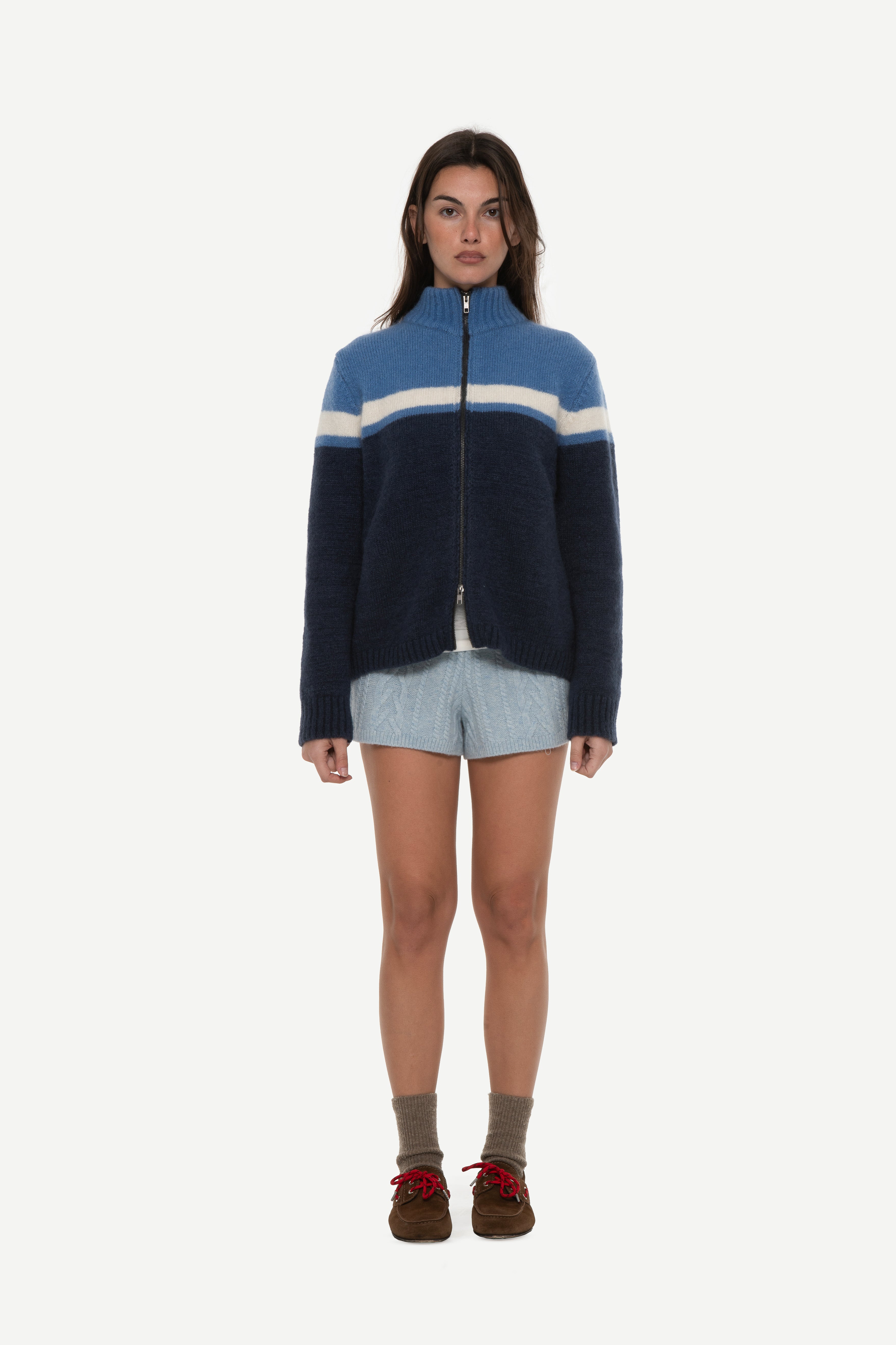 front view of woman wearing a mohair zip cardigan with two shades of blue and white stripe at chest and blue shorts on a white background
