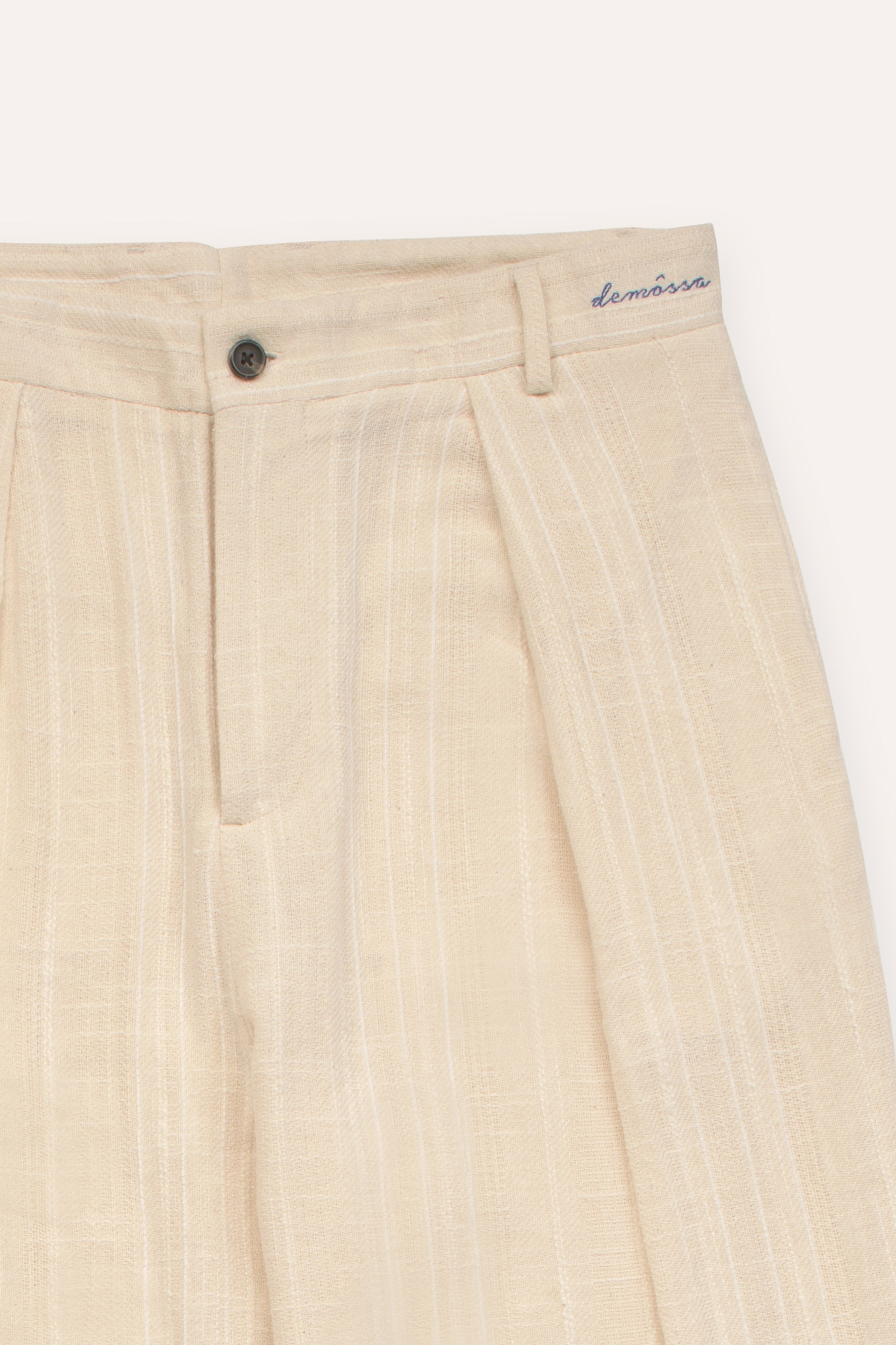 Cream pleated pants with a embroided "demossa" logo on a white background