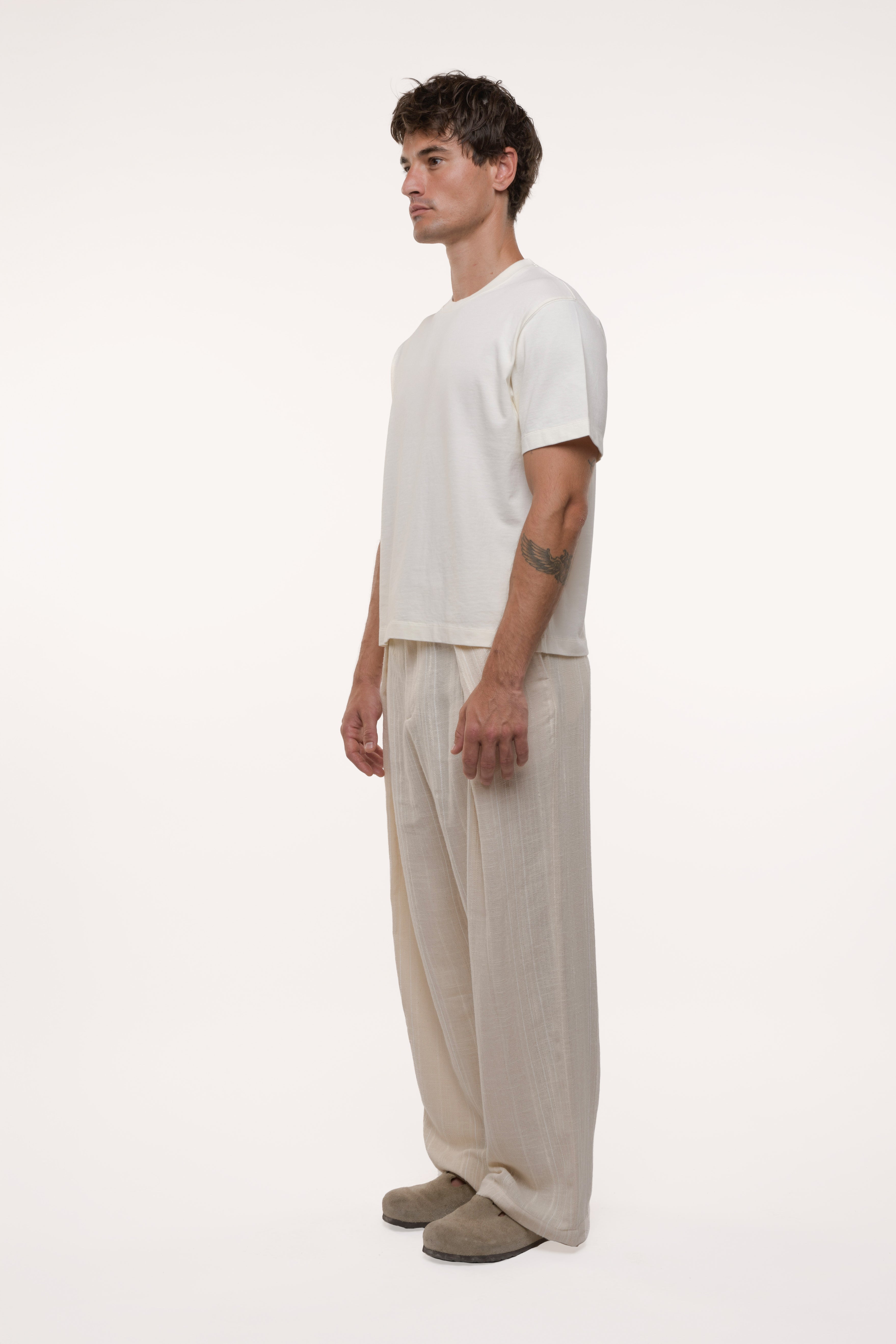 Side view of a man wearing a white t-shirt and beige pleated pants on a white background