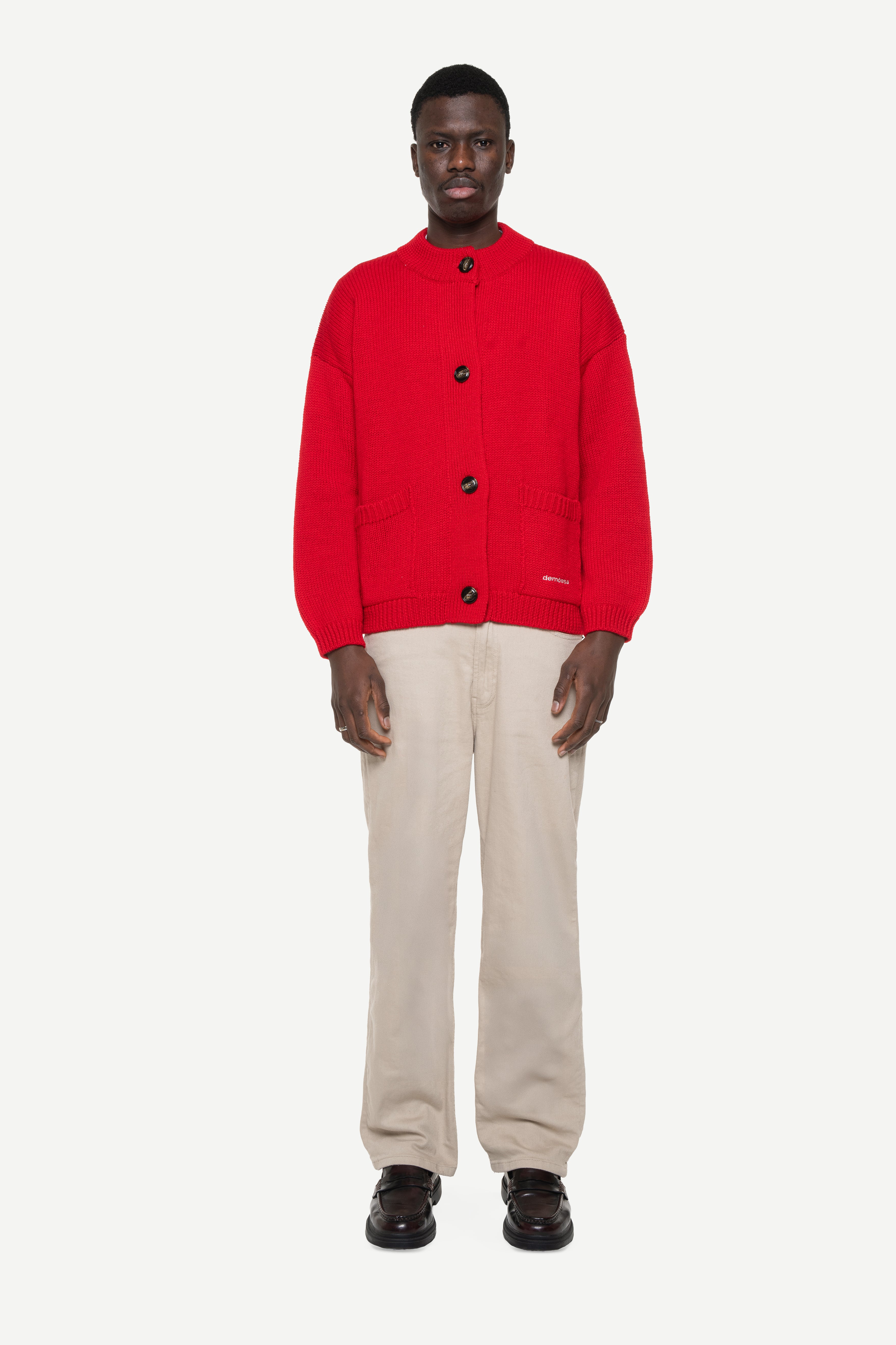 man wearing a red buttoned cardigan with two front pockets and beige jeans on a white background