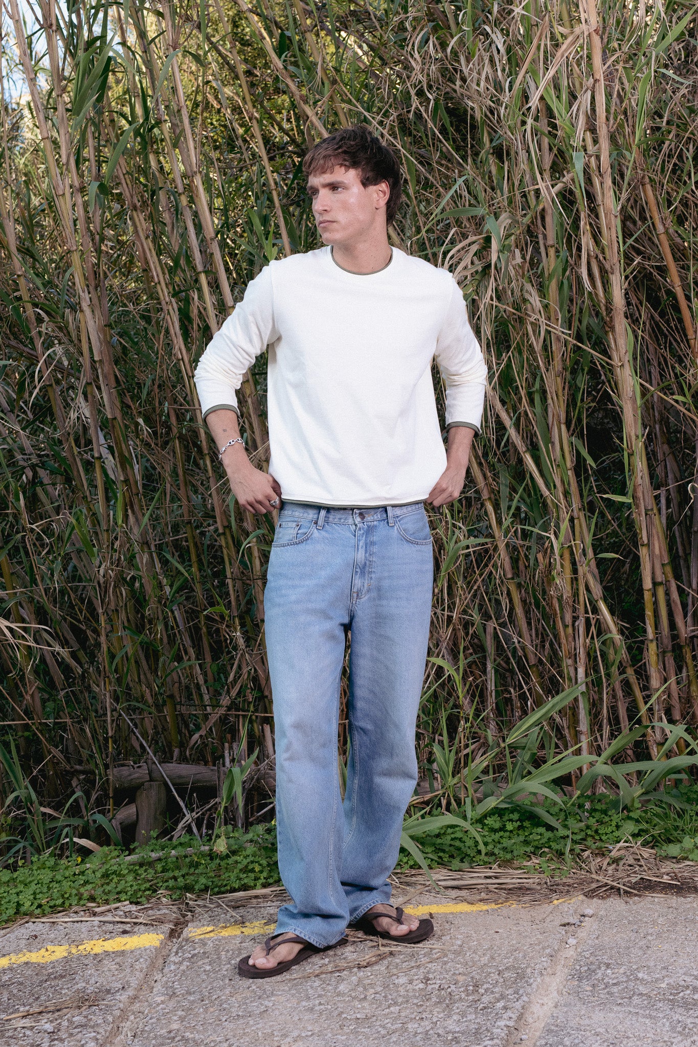 Man wearing a white shirt and blue jeans standing in front of tall grasses.