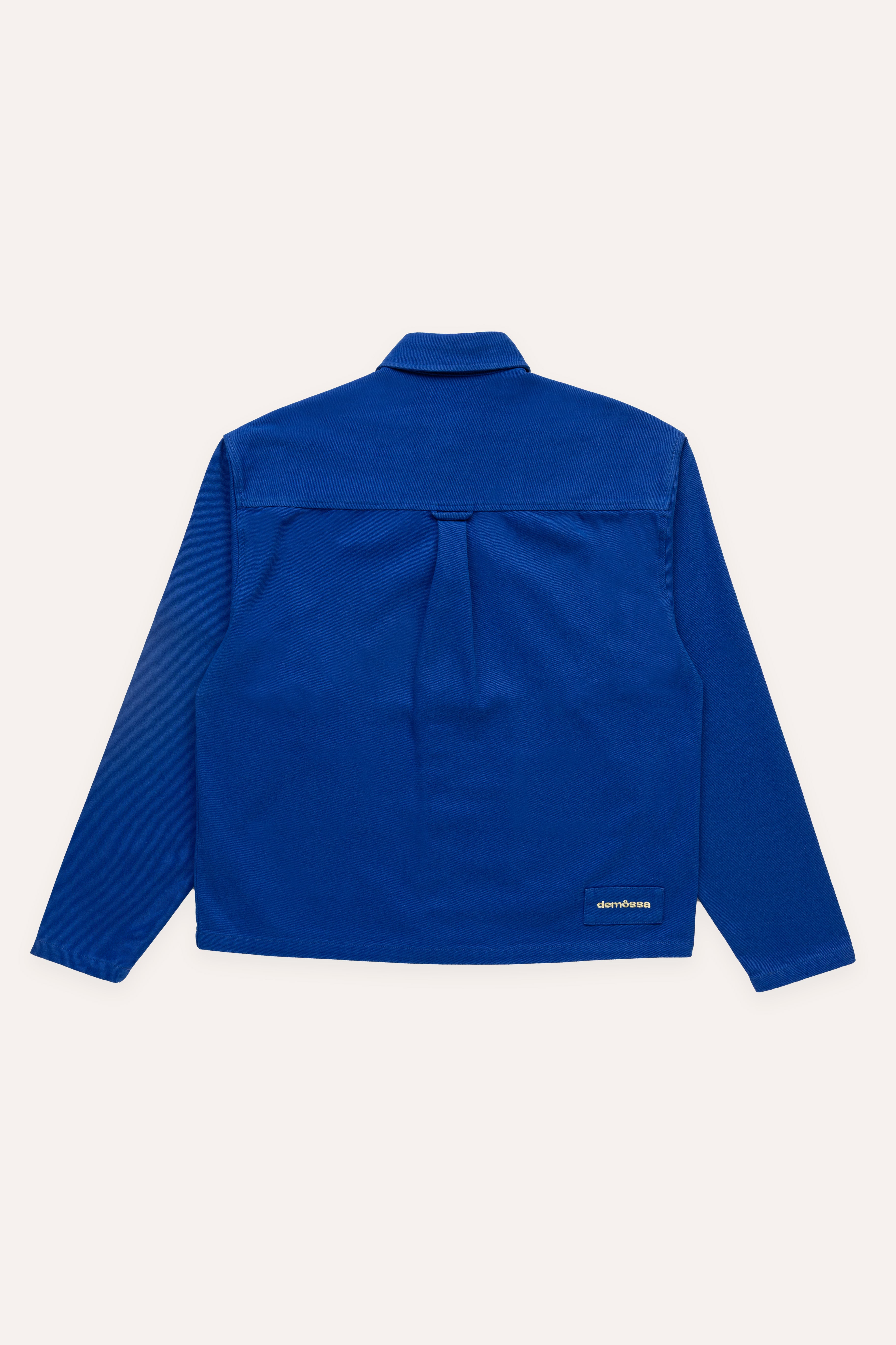 Flat lay back view of blue overshirt featuring a small Demossa logo patch near the bottom hem