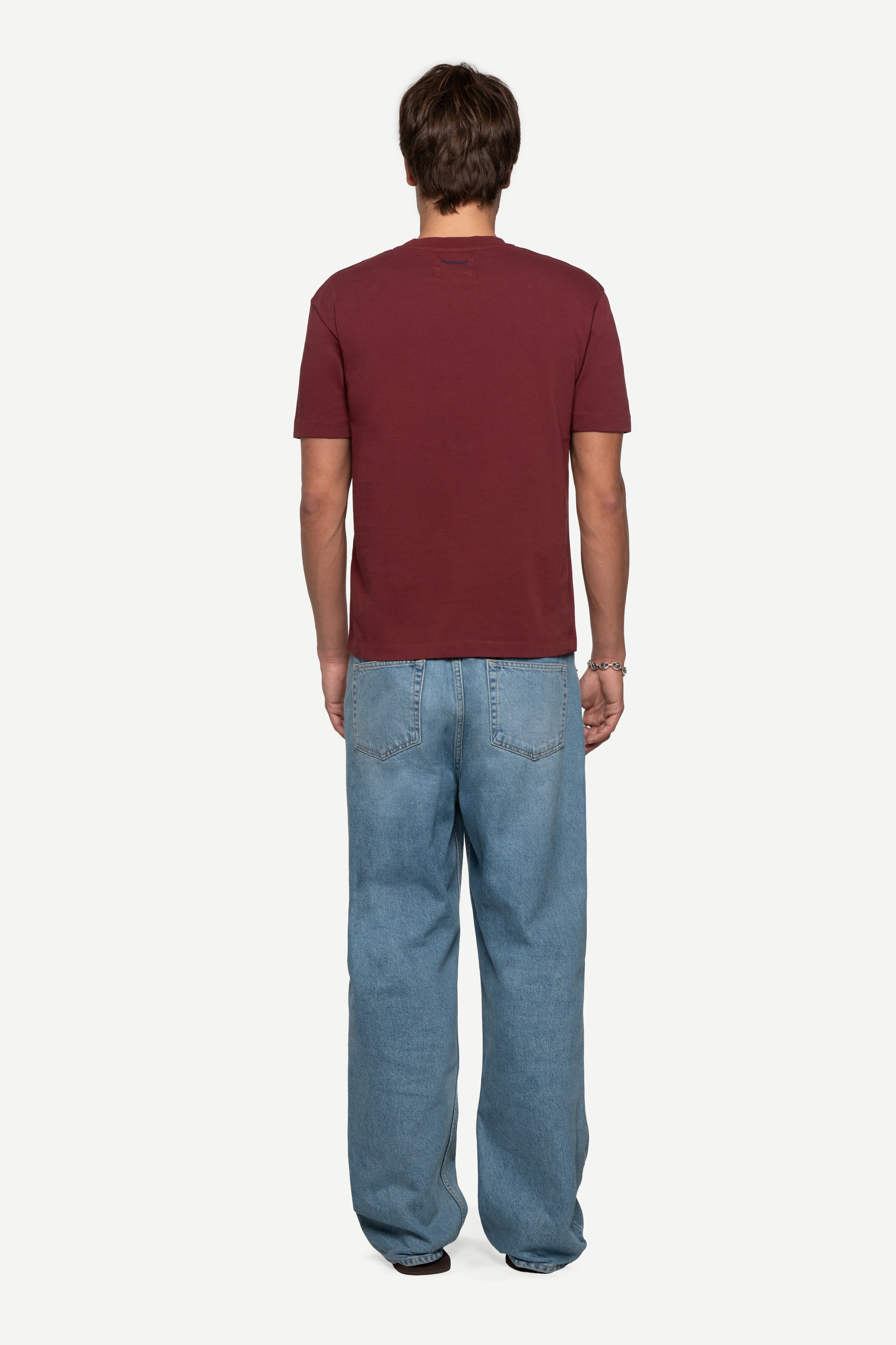back view of man wearing a regular fit short-sleeved burgundy t-shirt with blue jeans on a white background