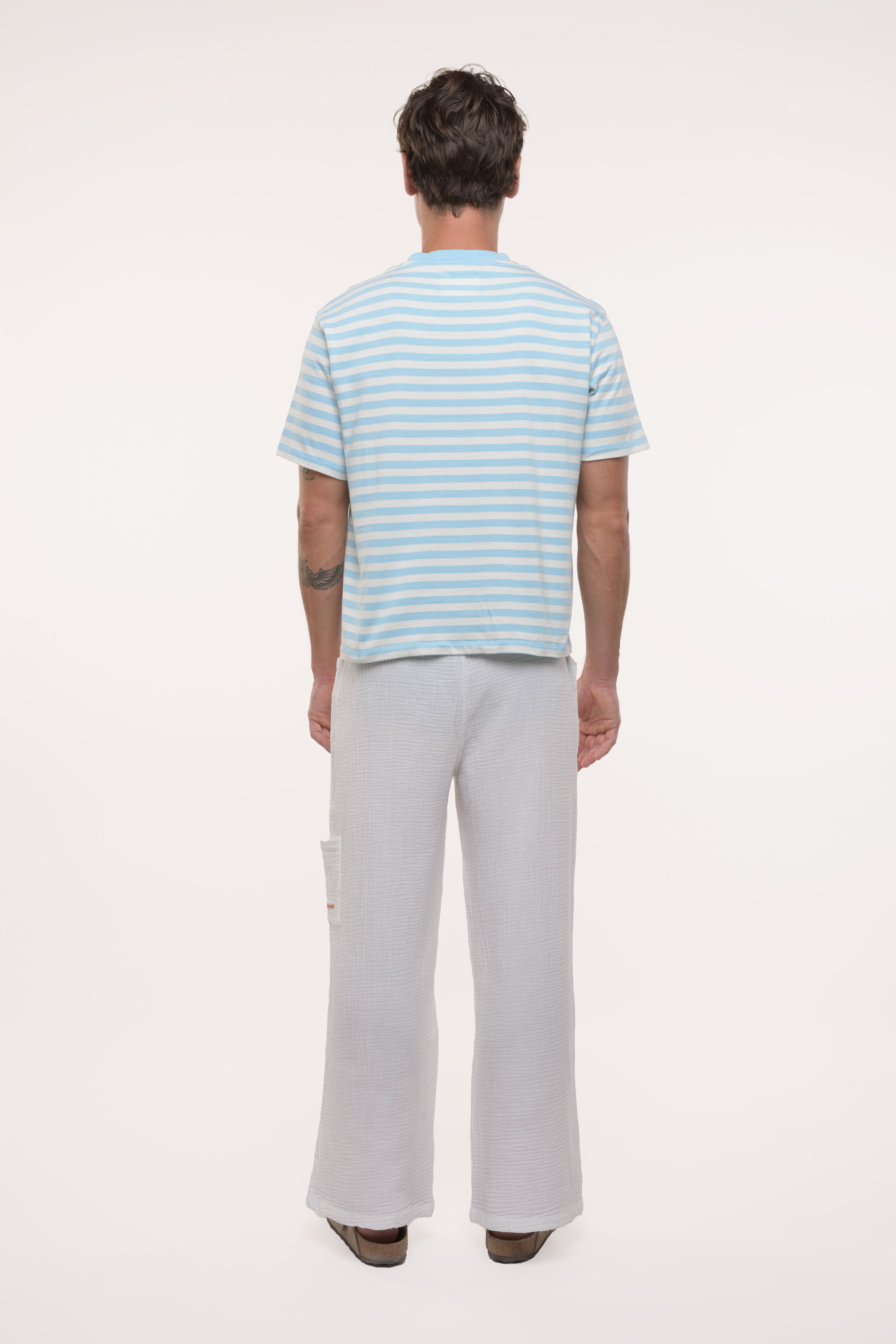 Back view of a man wearing a striped shirt and light gray pants on a white background