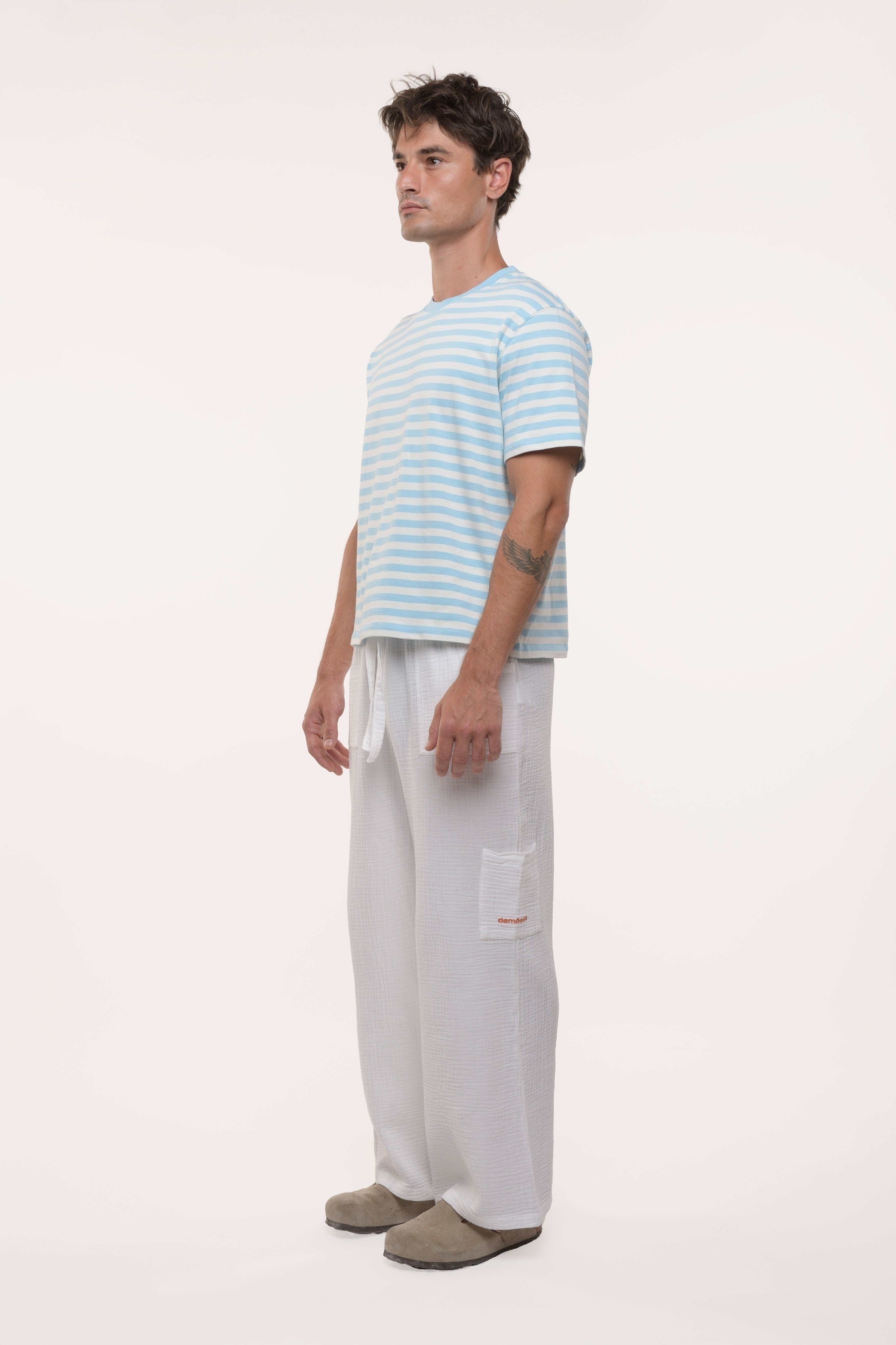 Side view of a man wearing a light blue striped t-shirt and white pants on a white background