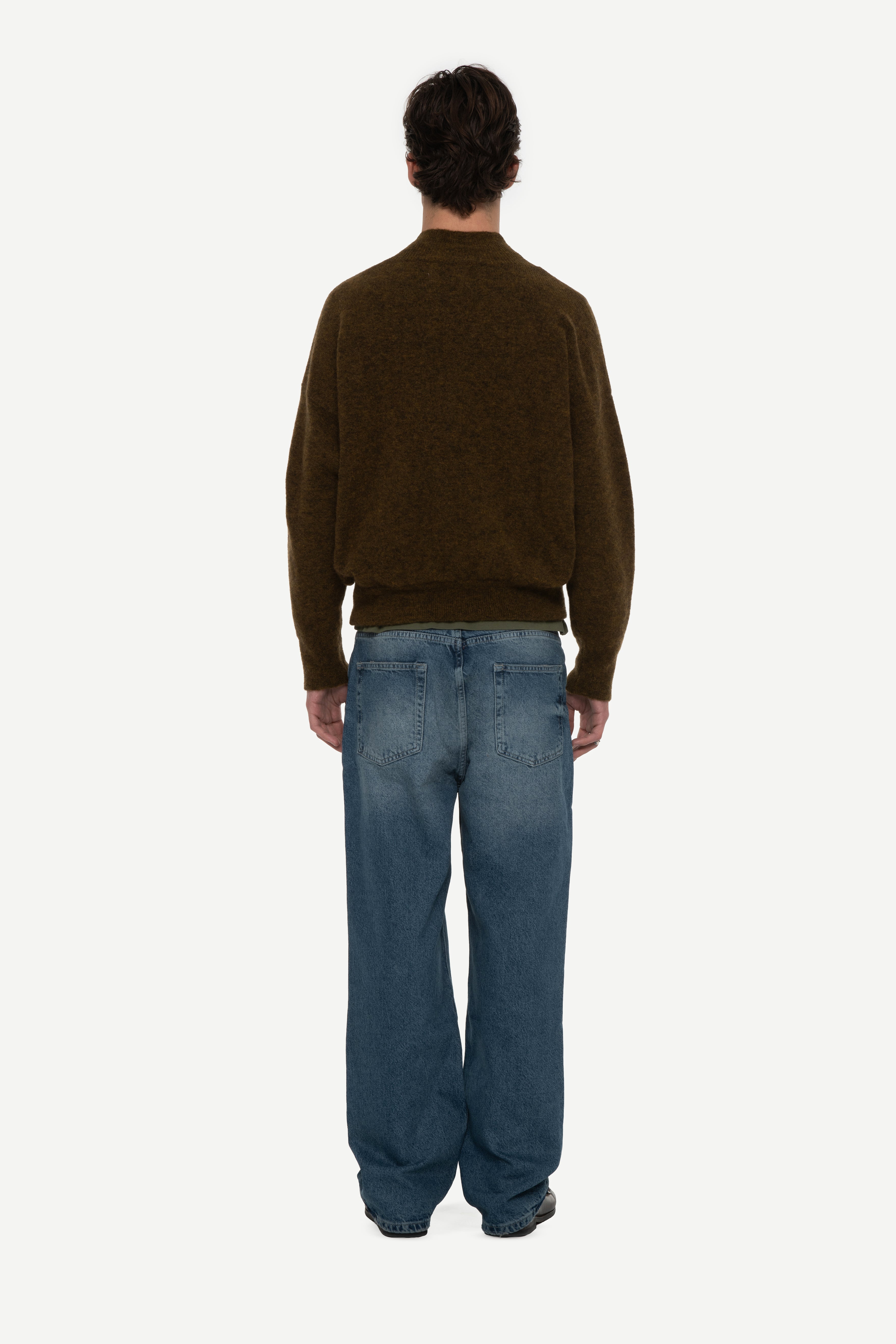 back view of man wearing a olive mockneck sweater and blue jeans on a white background