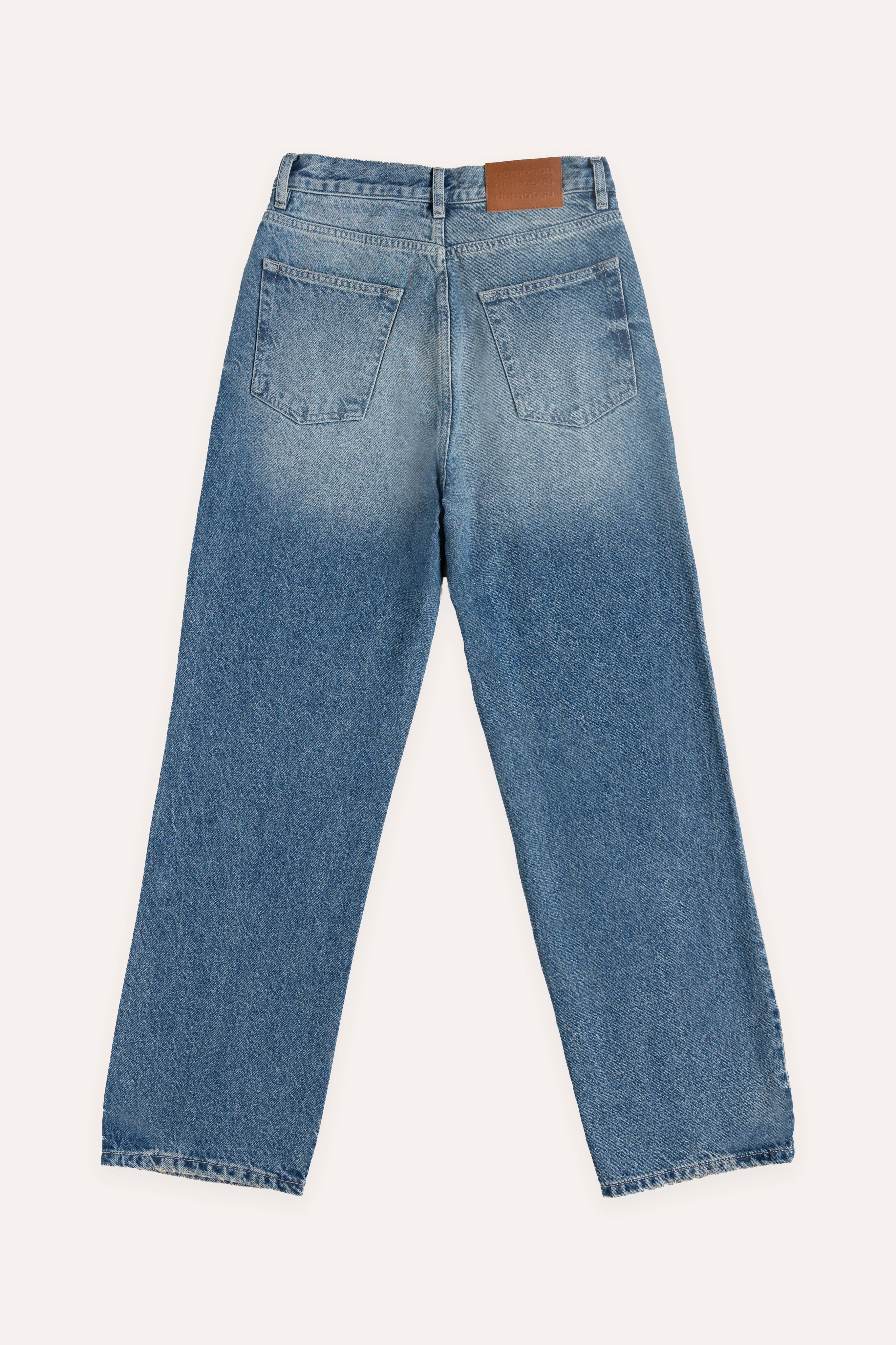 Flat lay back view of blue jeans with patch pockets and leather jacron on waistband