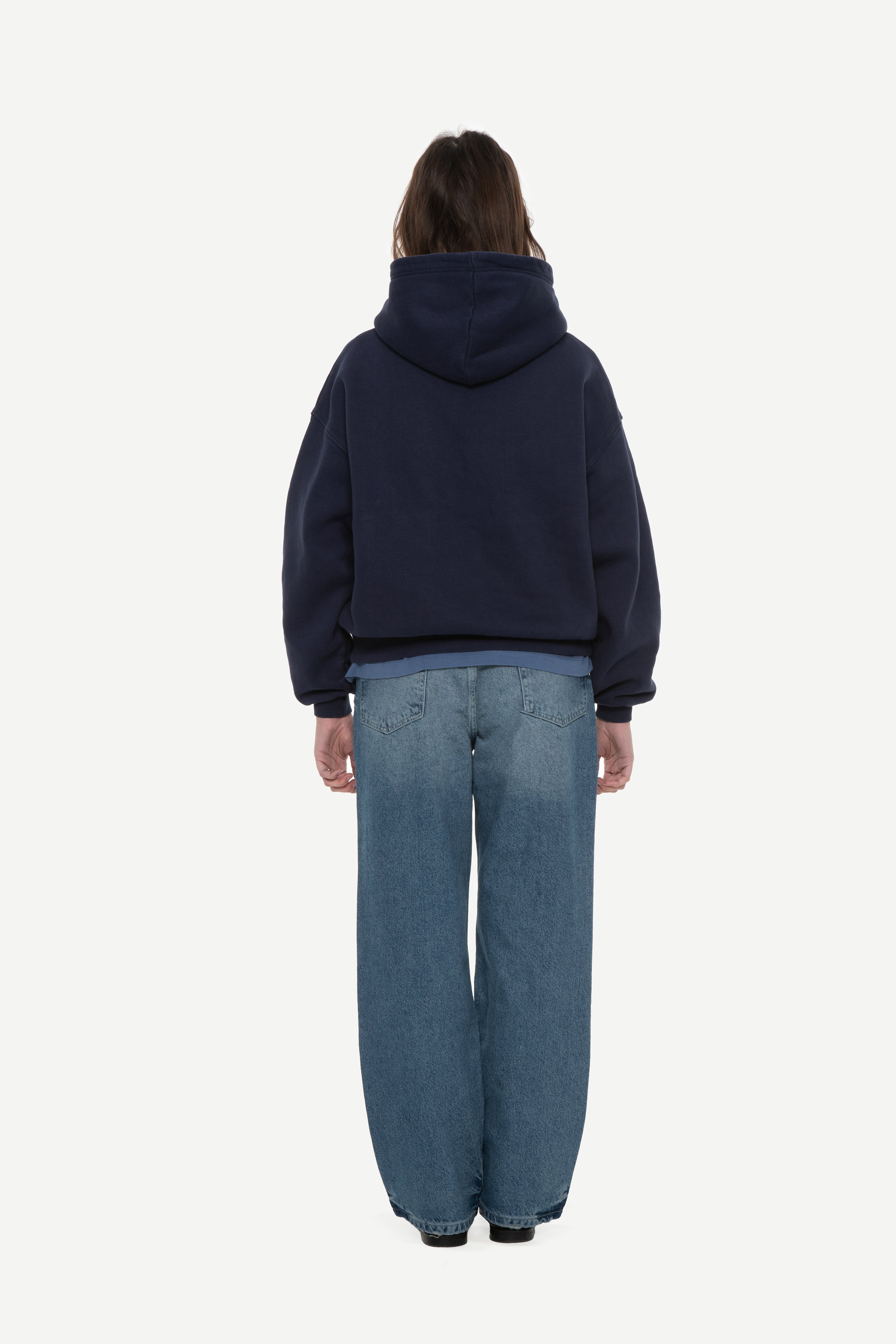 back view of woman wearing a navy hoodie and blue jeans on a white background