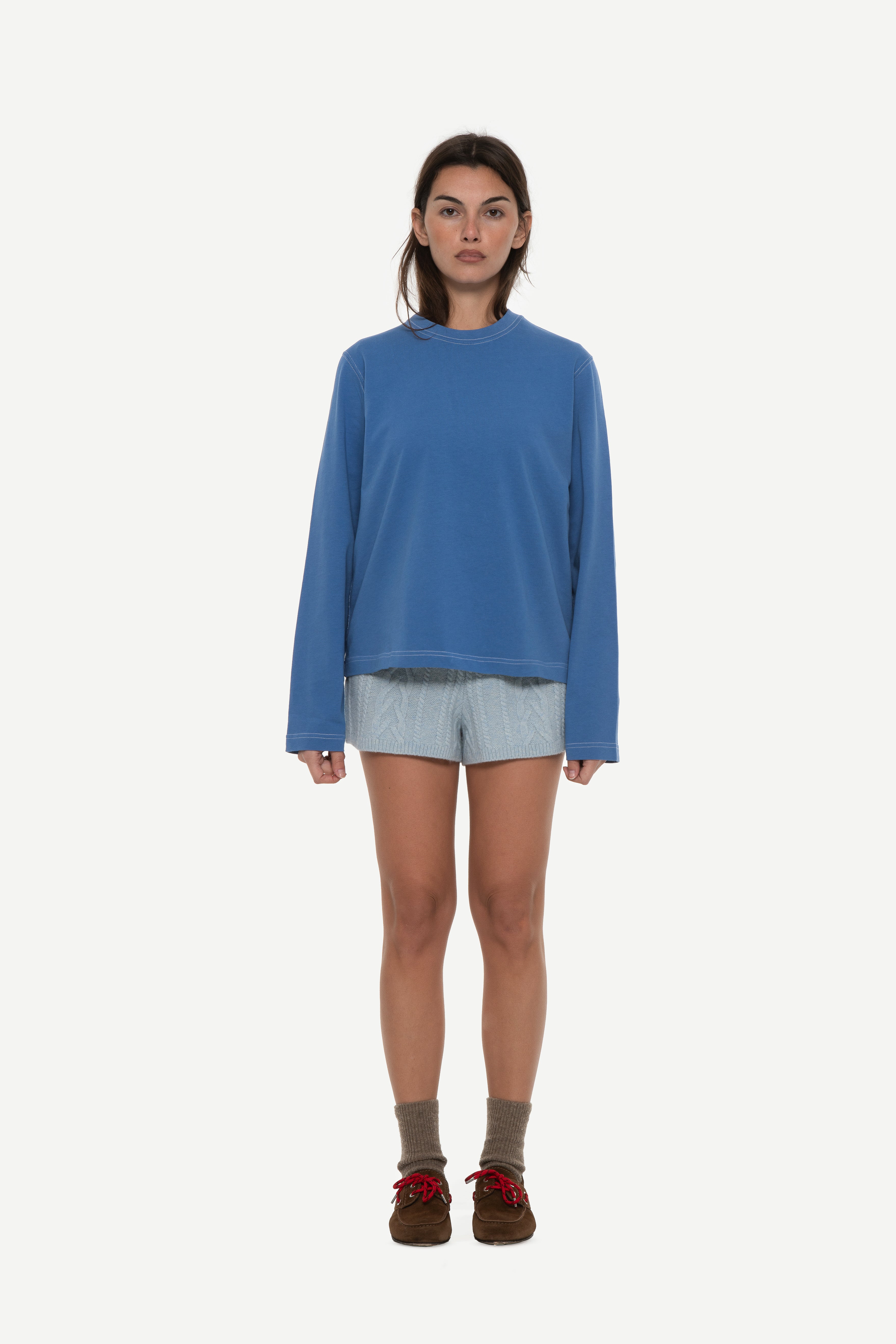 front view of woman wearing a blue long sleeve tee with contrast stitching and blue shorts on a white background