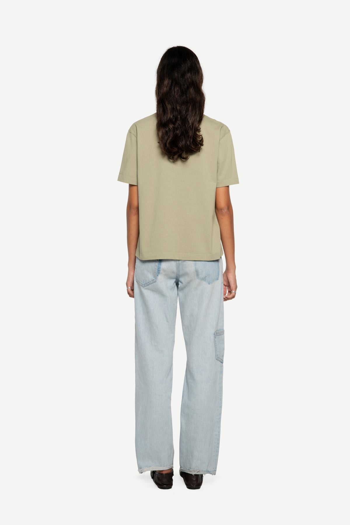 A model viewed from the back wearing a light green short-sleeve t-shirt and light blue wide-leg jeans against a plain white background.