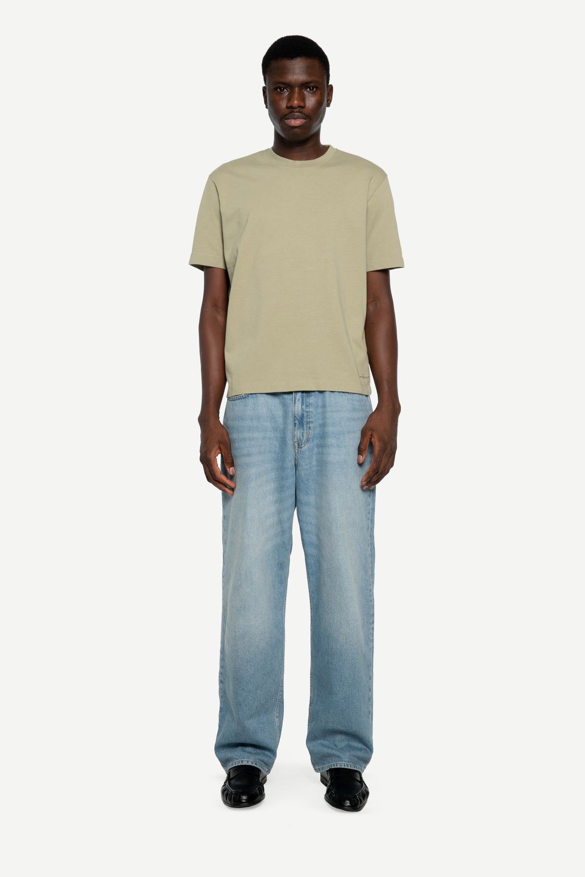 A man modeling a light green short-sleeve t-shirt and light blue relaxed-fit jeans against a plain light gray background.