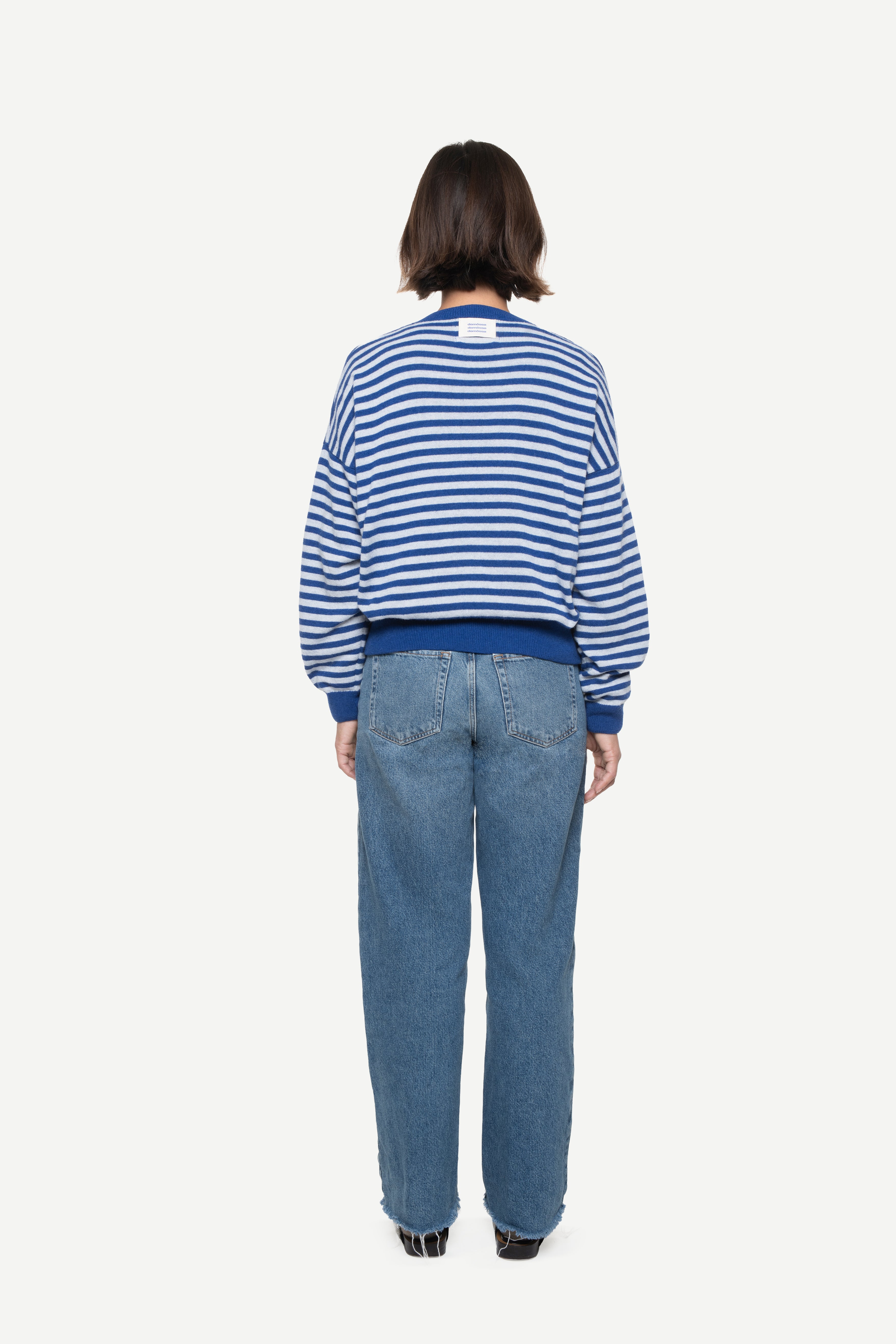 back view of a woman wearing a blue knit striped sweater with demossa label and jeans on a white background