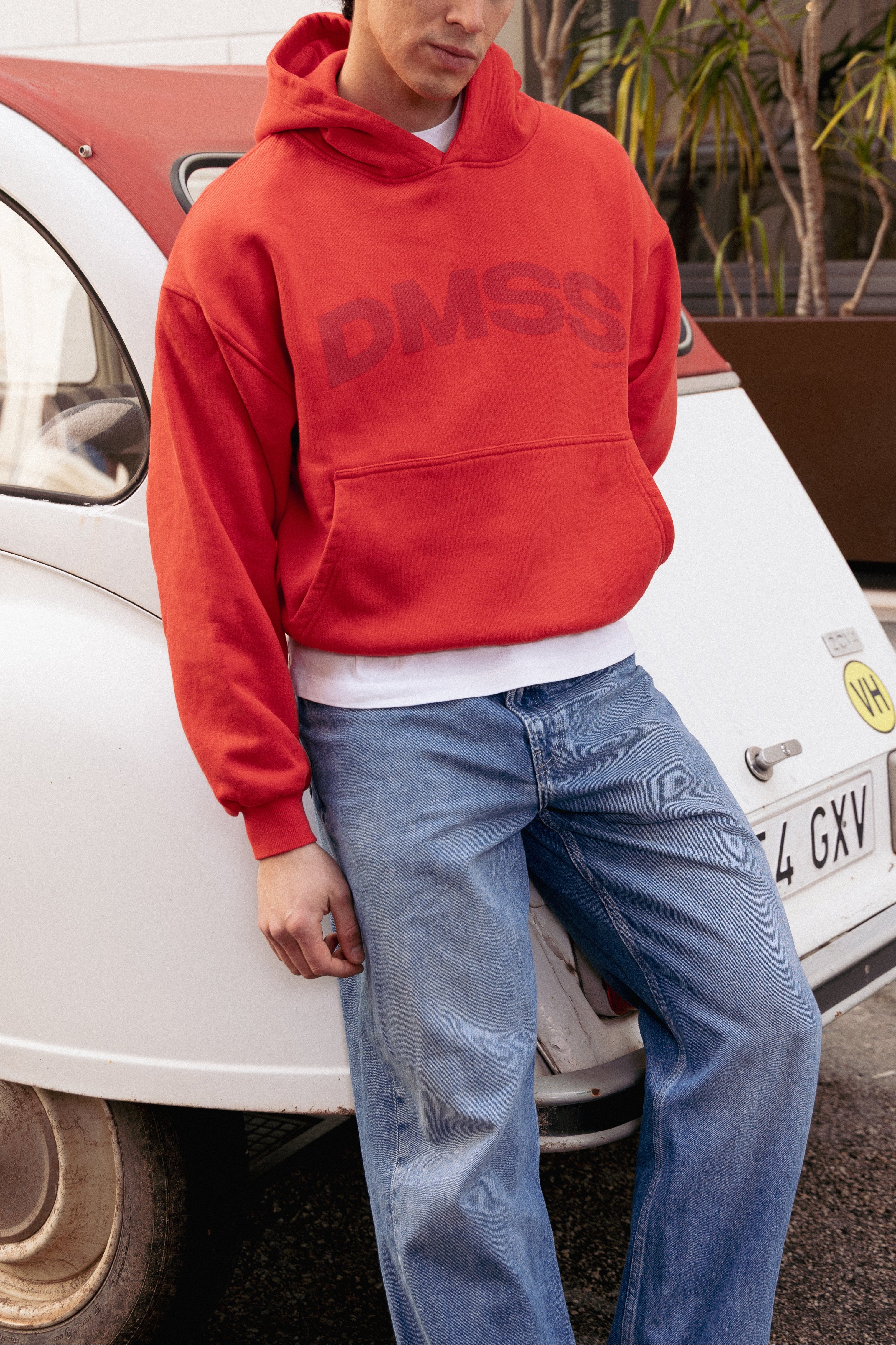 Person wearing a red hoodie with 'DMSS' logo standing next to a white car.