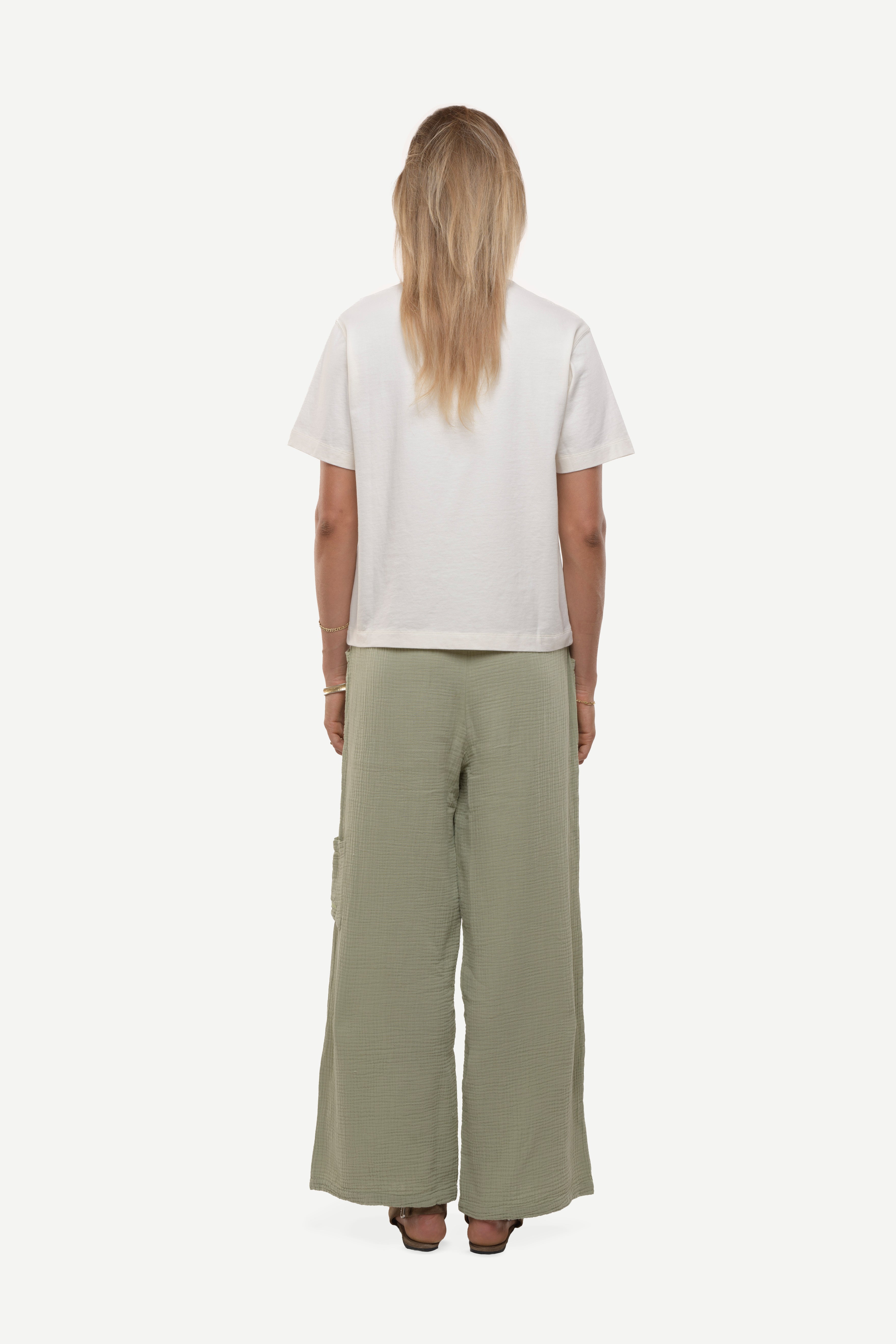 Back view of woman wearing a white t-shirt with red collar rib and green cotton pants white background