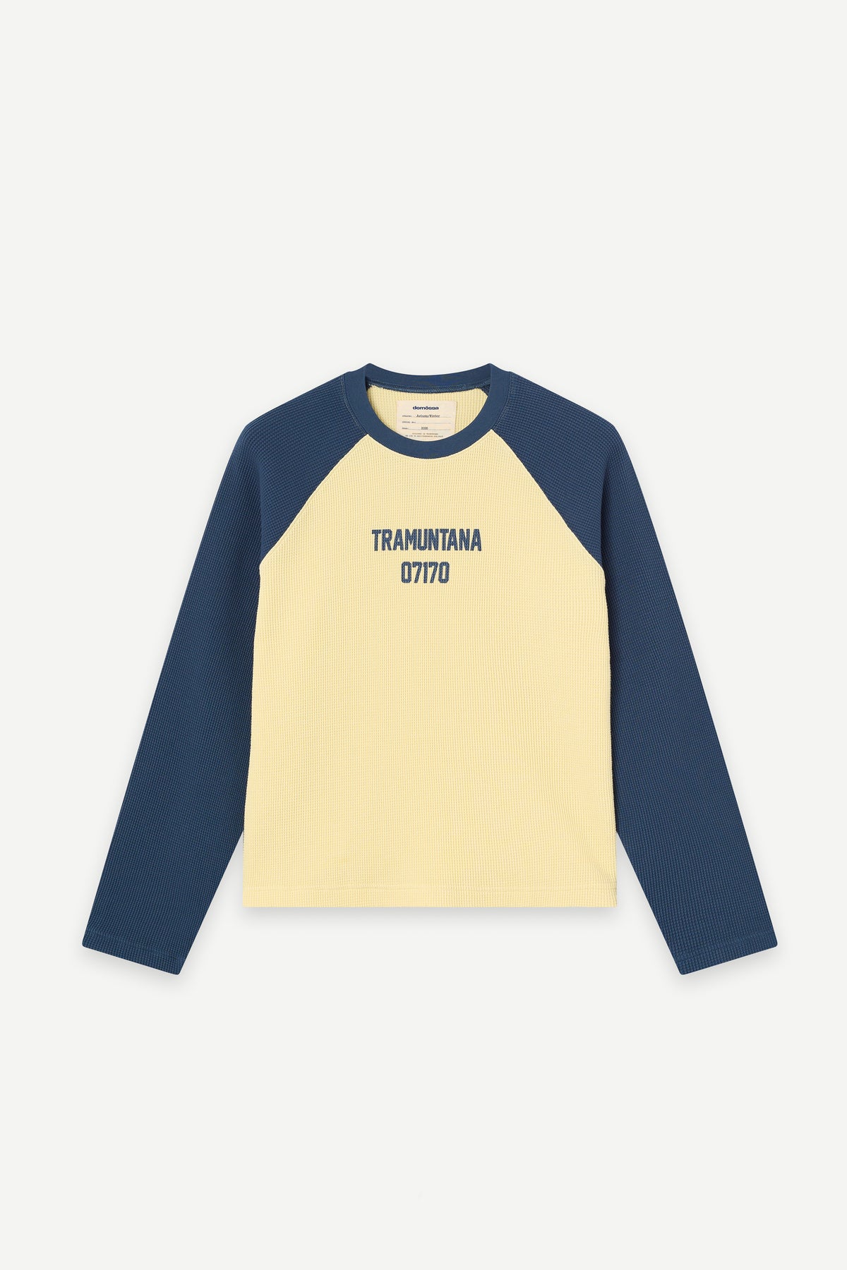 A long-sleeve waffle raglan t-shirt with a cream-colored body and navy blue sleeves, featuring the text 'TRAMUNTANA 07170' printed in navy on the chest, displayed against a light gray background.