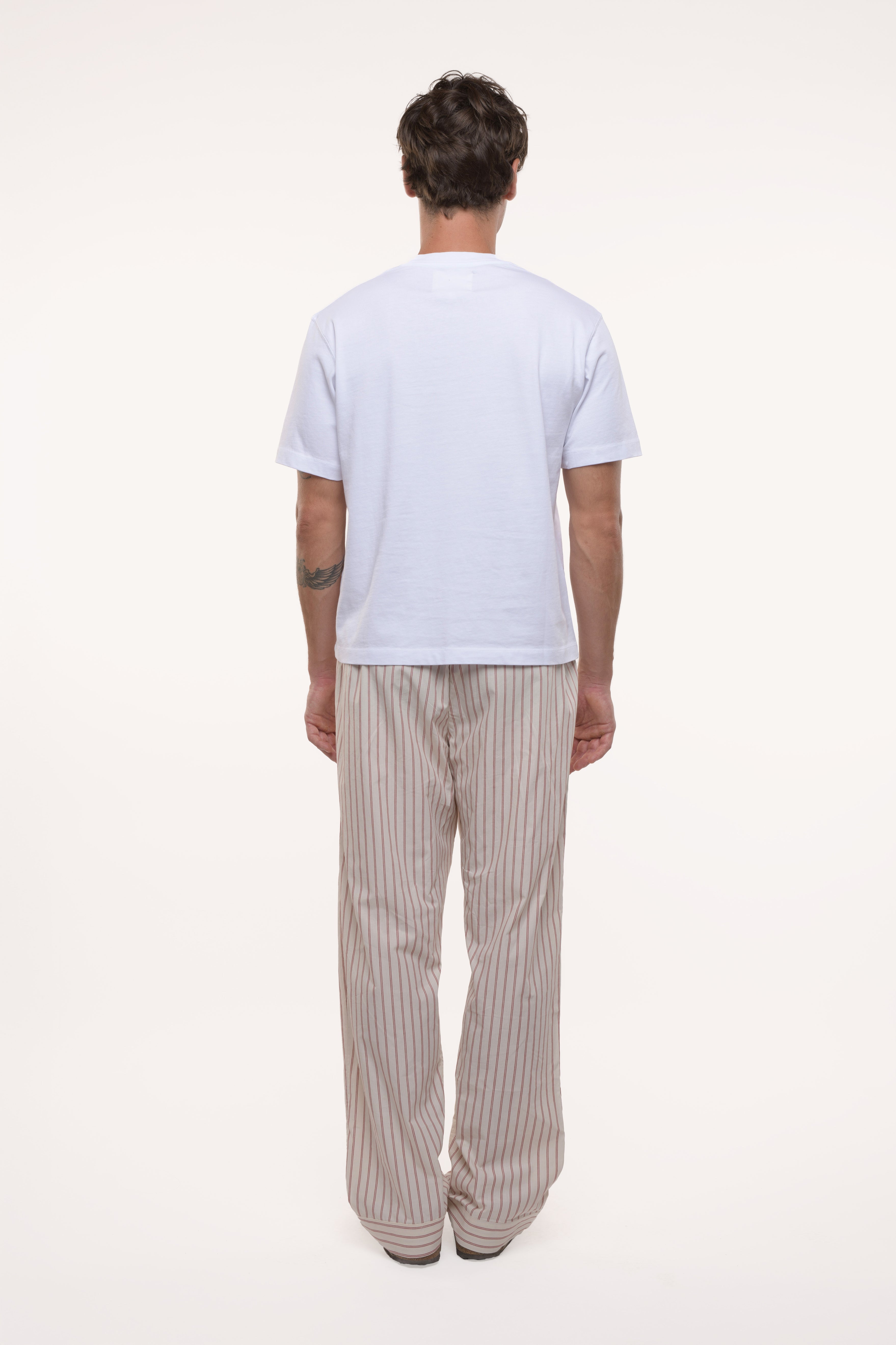 Back view of a man wearing a white t-shirt and beige striped pants on a white background