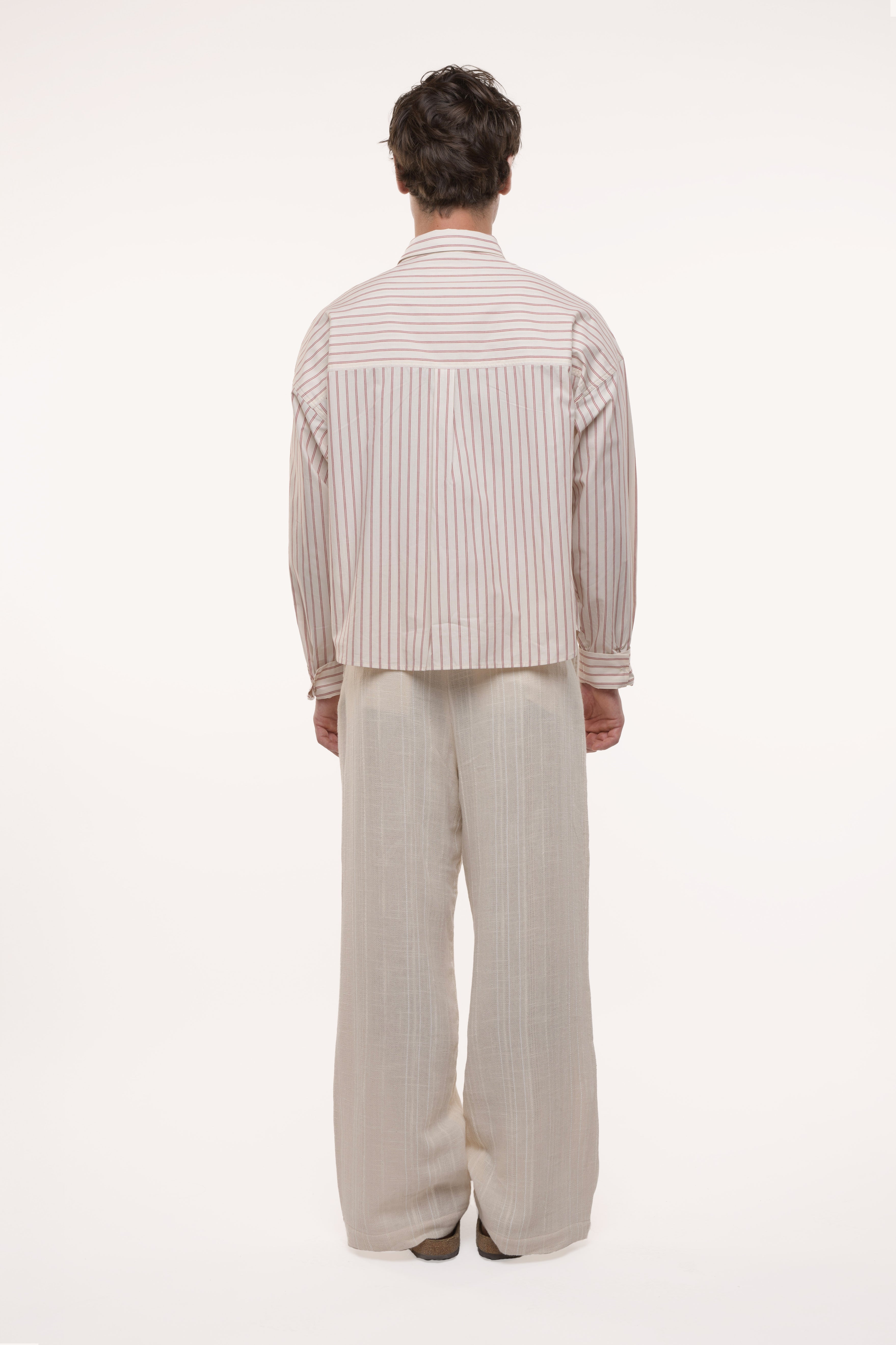 Back view of a man wearing a striped shirt and beige pants on a white background