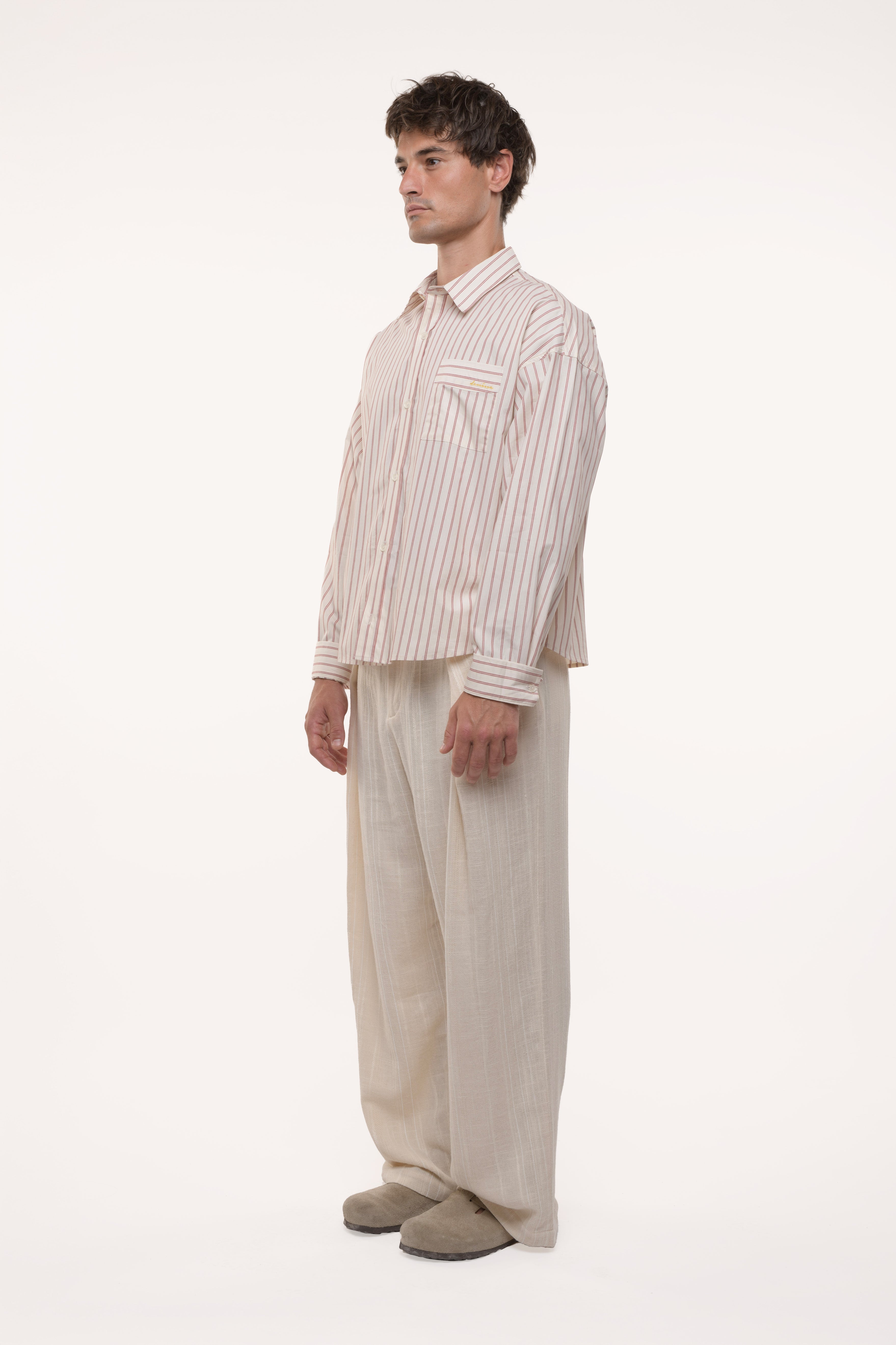 Side view of a man wearing a striped shirt and beige pants on a white background