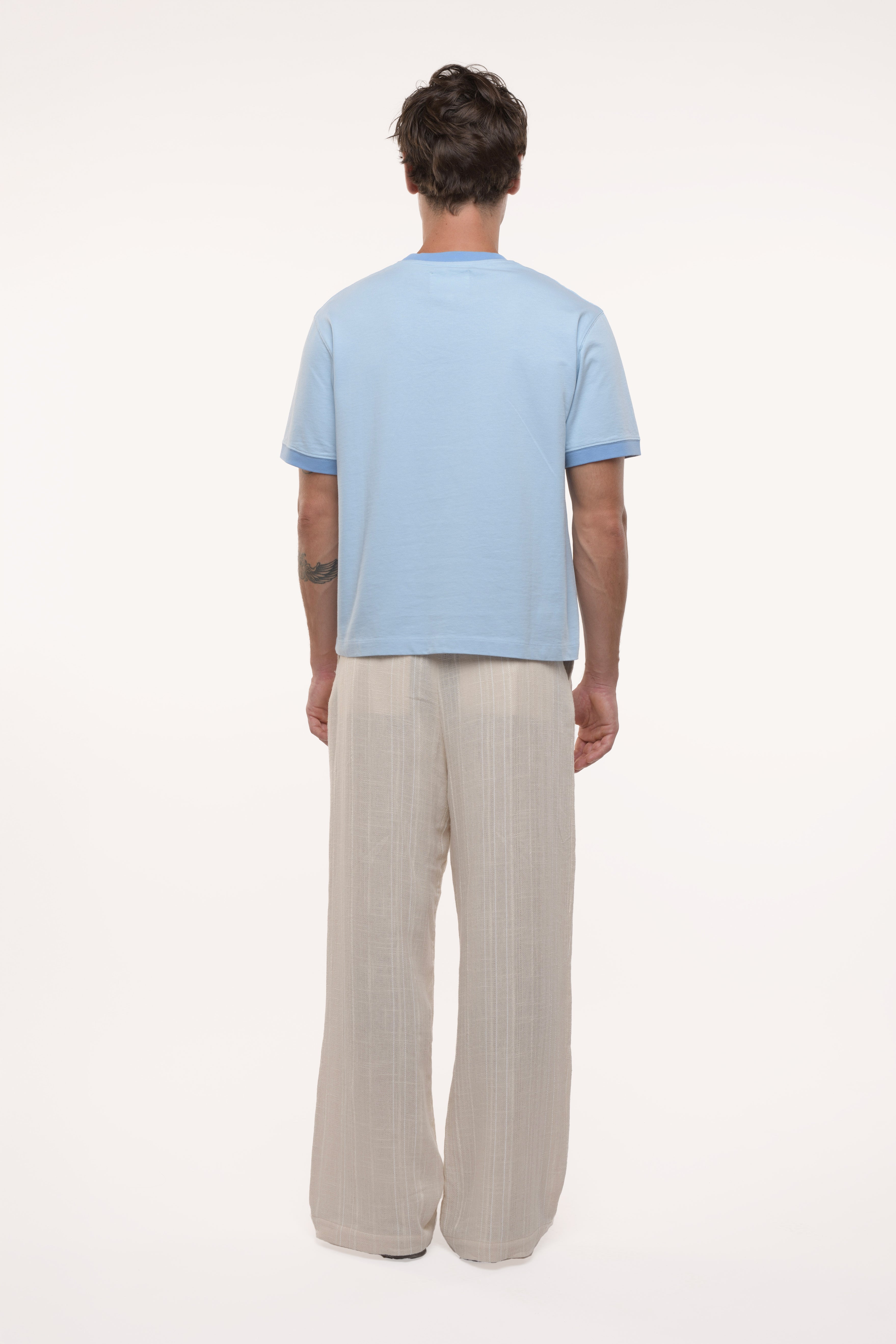 Back view of a man wearing a light blue t-shirt and beige pants on a white background