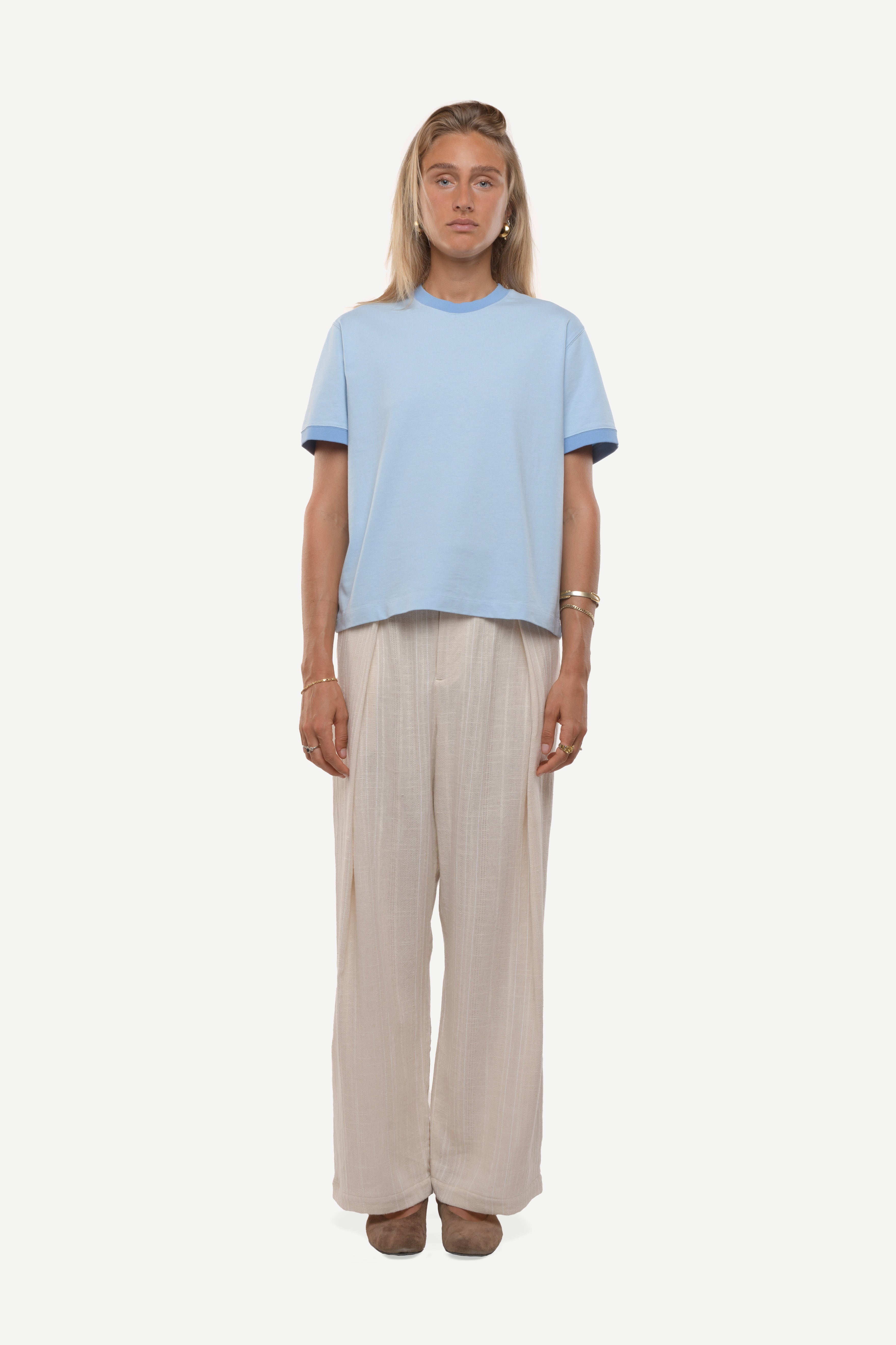 Woman wearing a light blue t-shirt with contras ribs and beige pants on a white background
