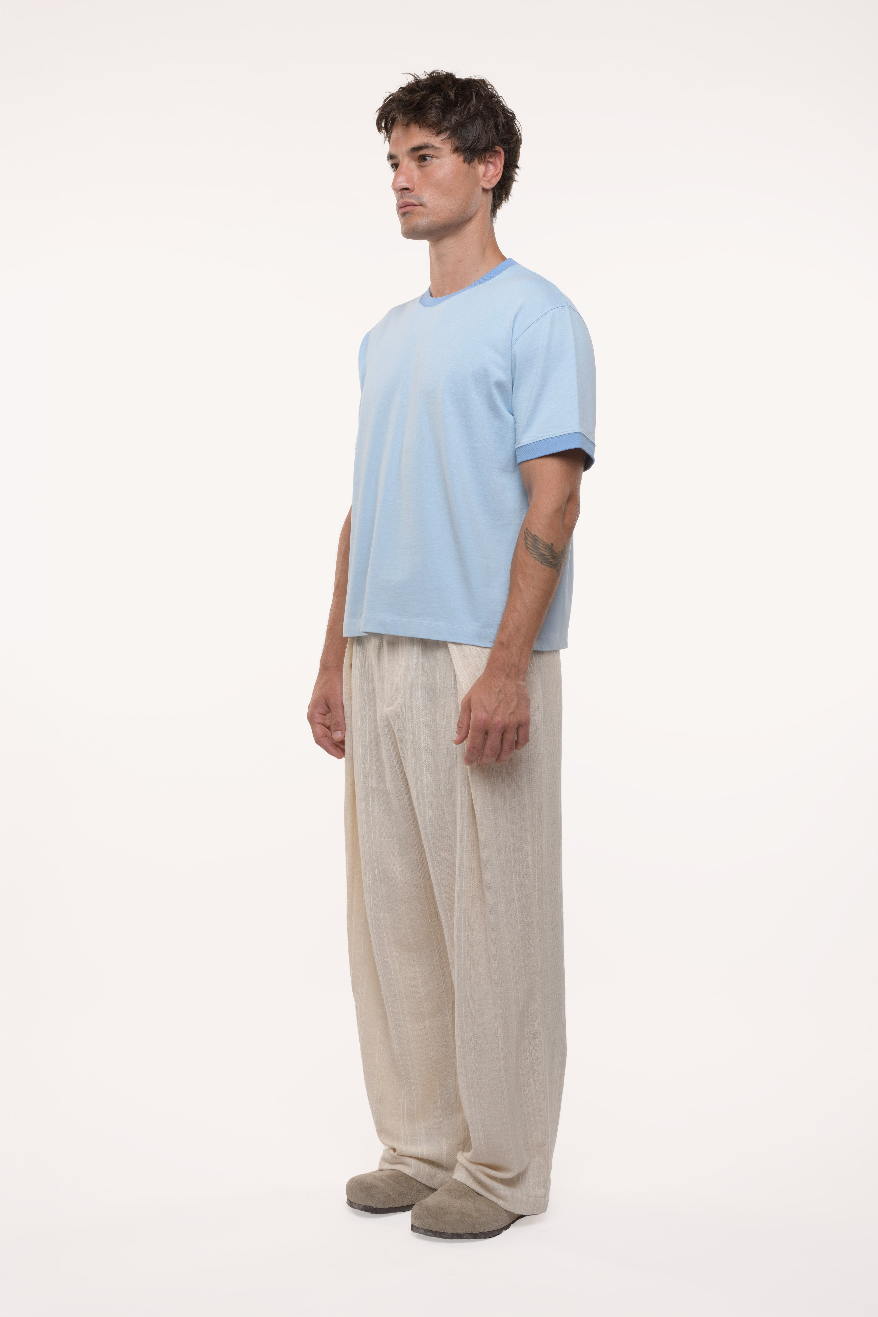 Side view of a man wearing a light blue t-shirt and beige pants on a white background