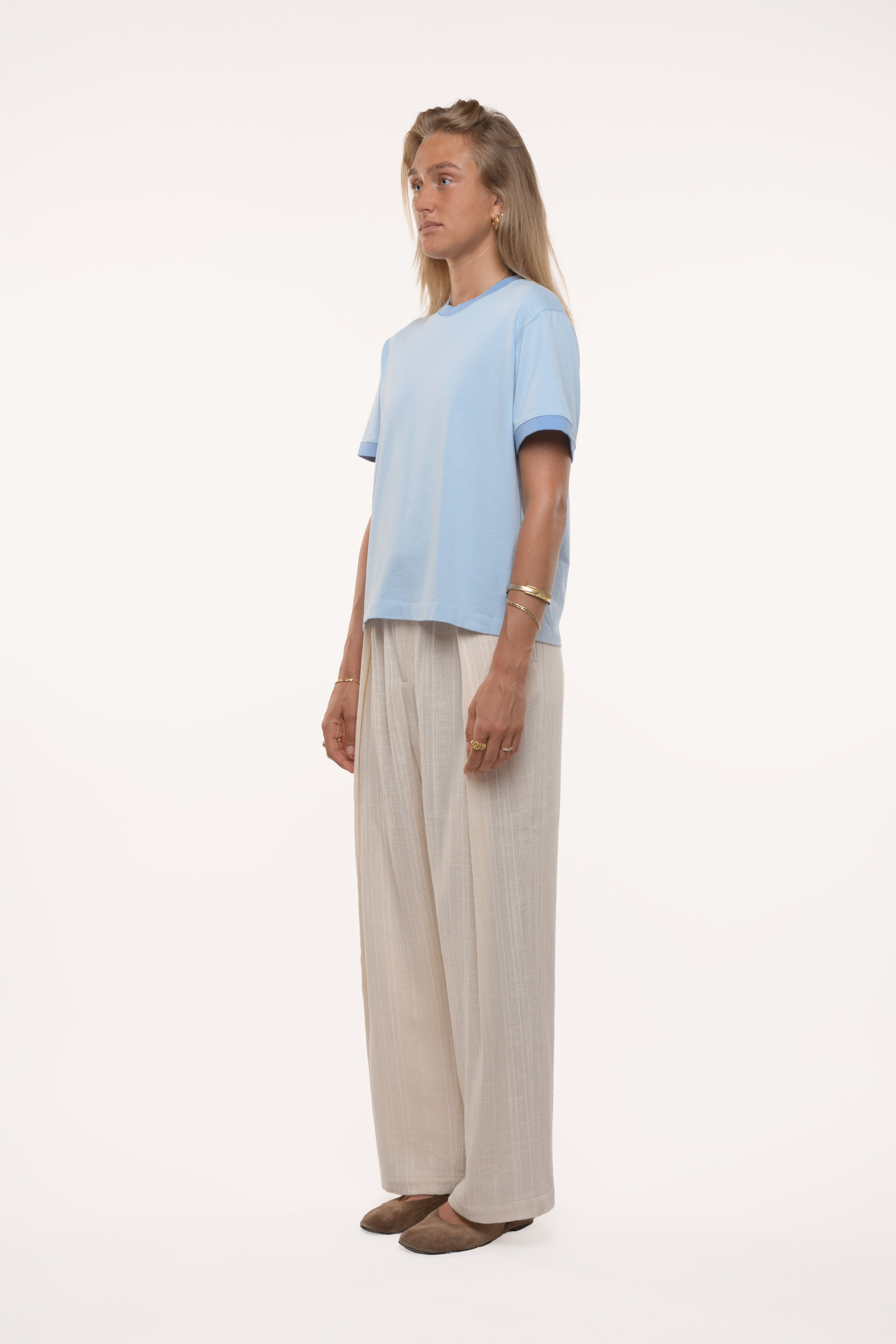 Side view of a woman wearing a light blue top and beige pants on a white background