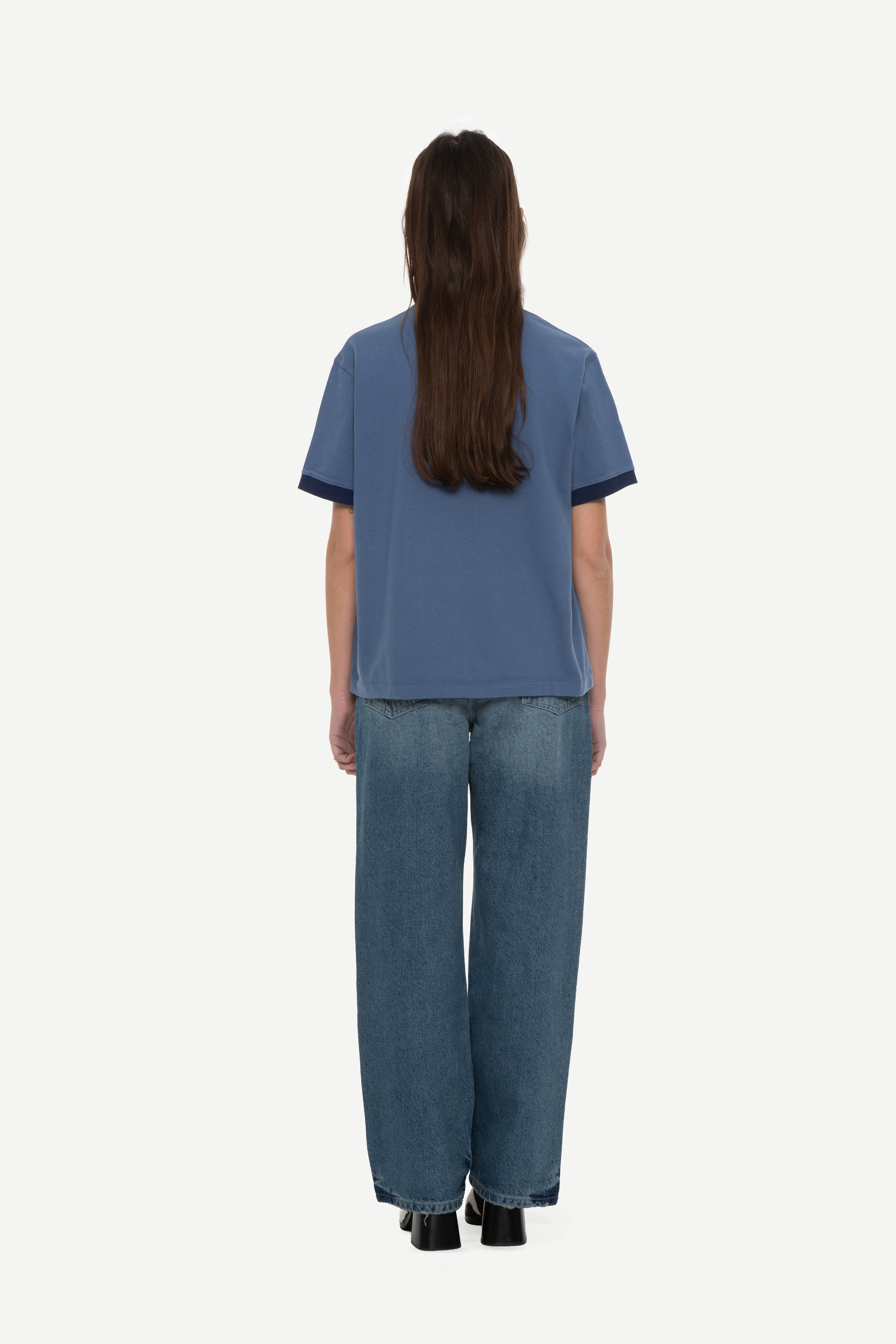 back view of woman wearing a navy t-shirt with contrast collar and arm rib and blue jeans on a white background