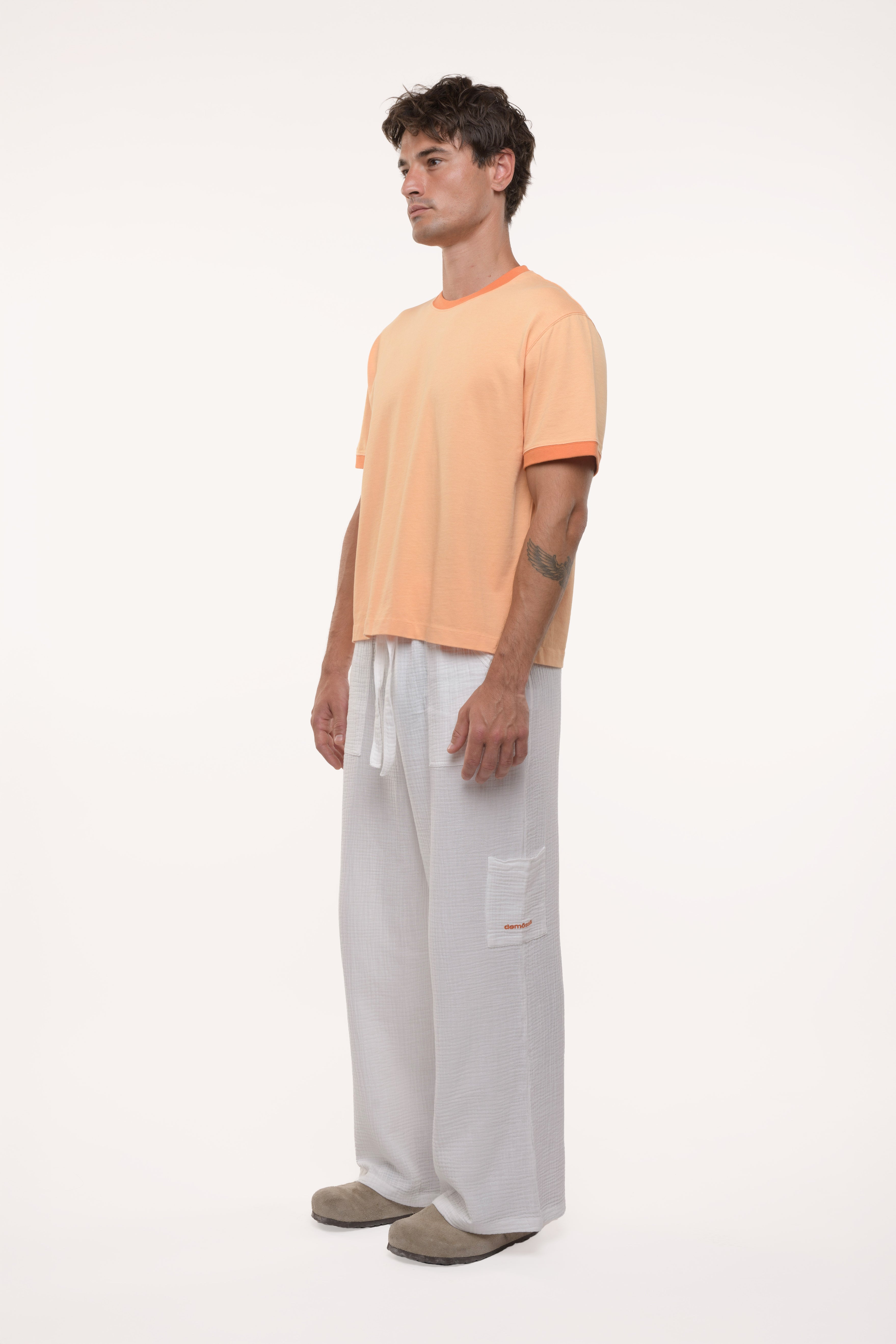 Side view of a man wearing an orange t-shirt and light gray pants on a white background