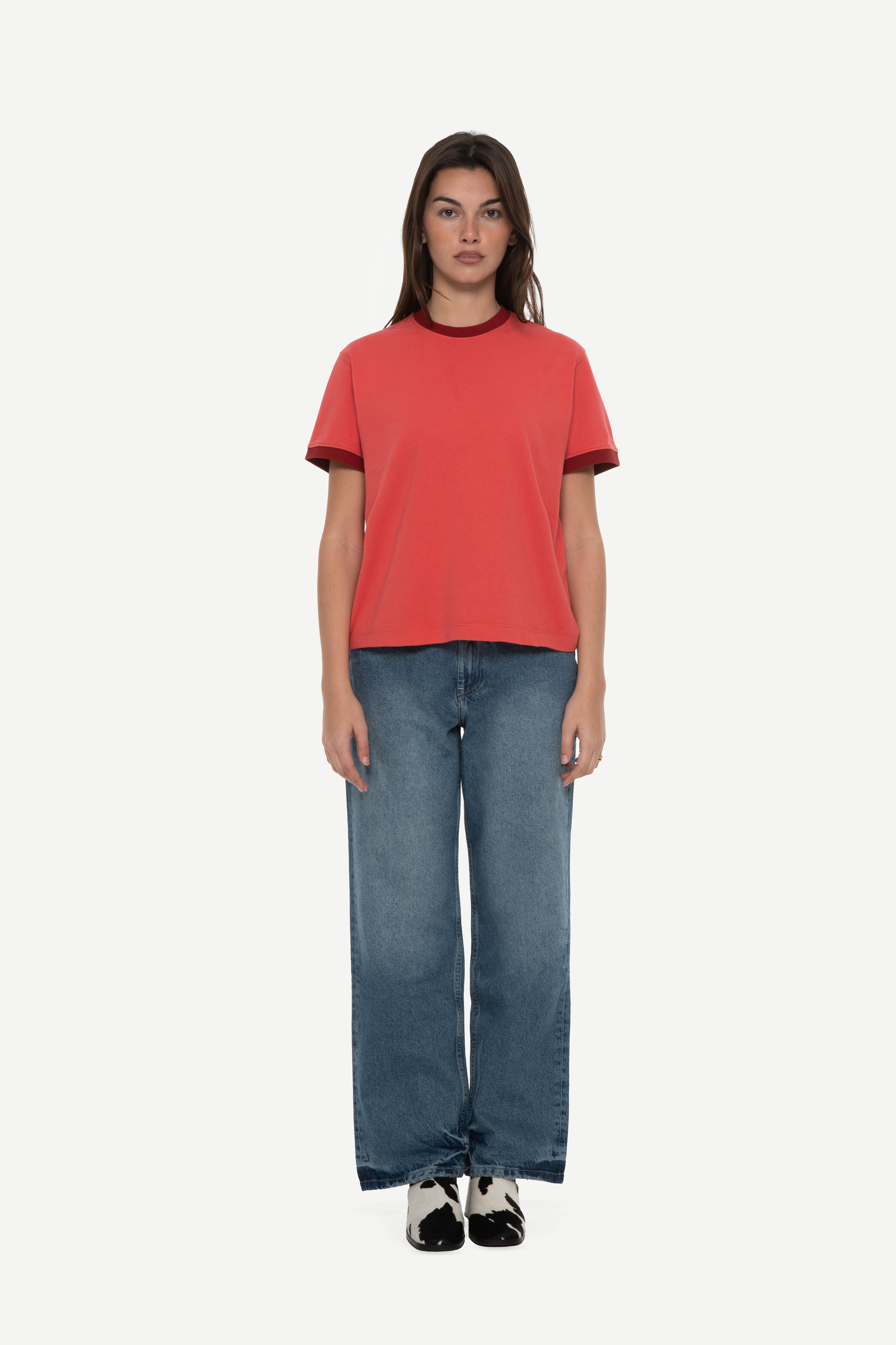 front view of woman wearing a red t-shirt with contrast collar and arm rib and blue jeans on a white background