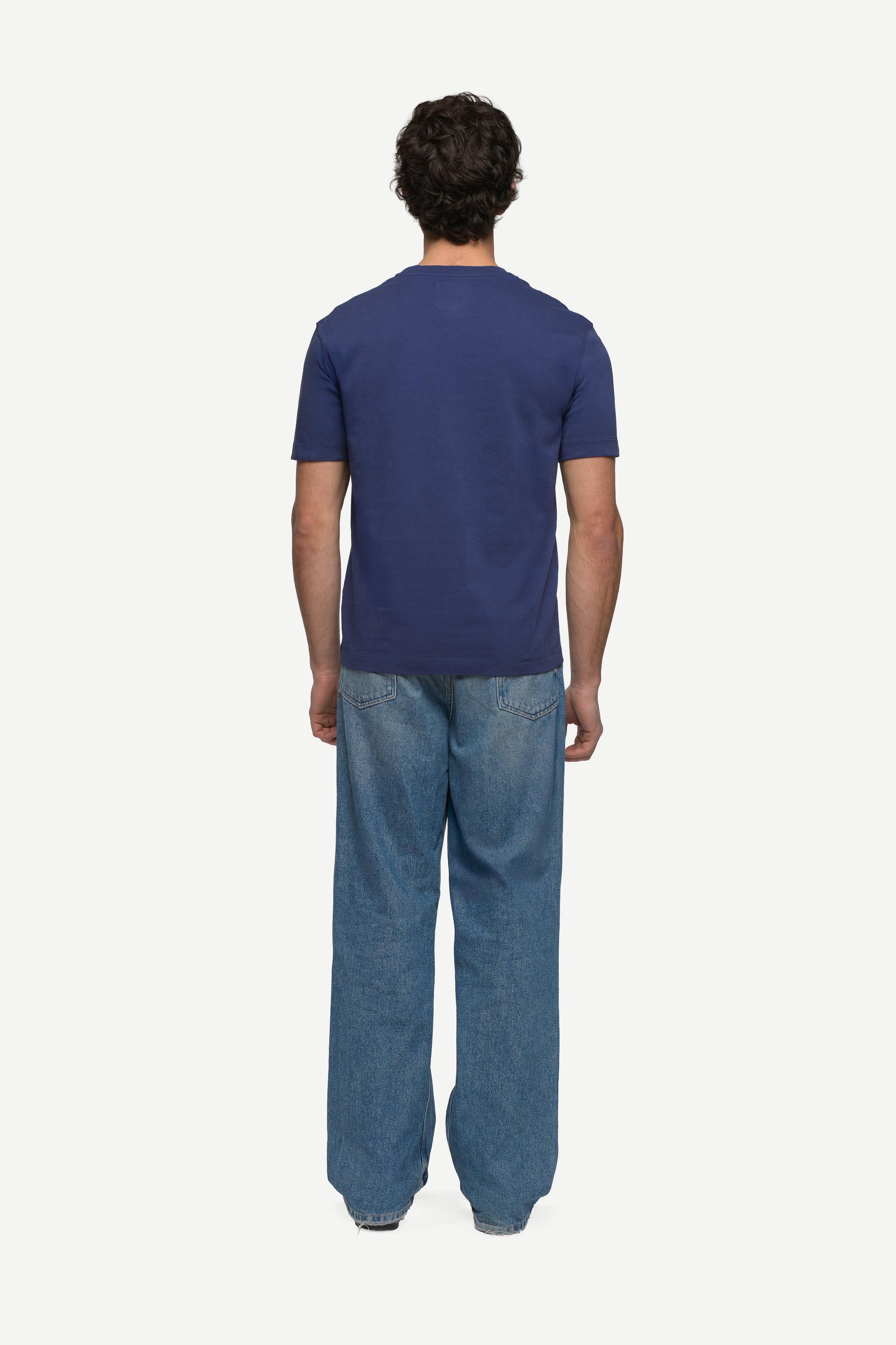 back view of man wearing a navy t-shirt and blue jeans on a white background