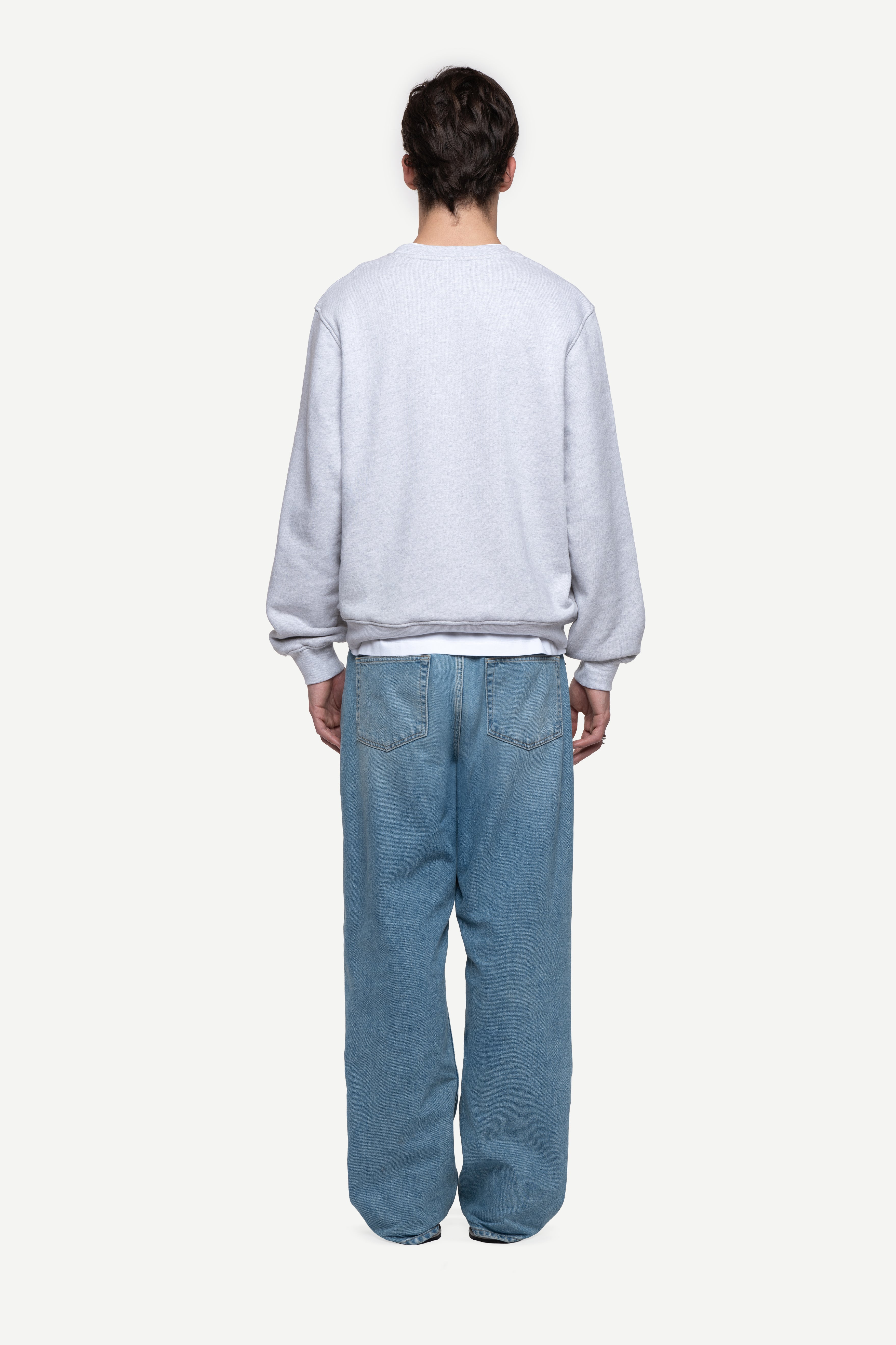back view of man wearing a melange grey relaxed-fit sweatshirt, blue jeans and flip flops on a white background