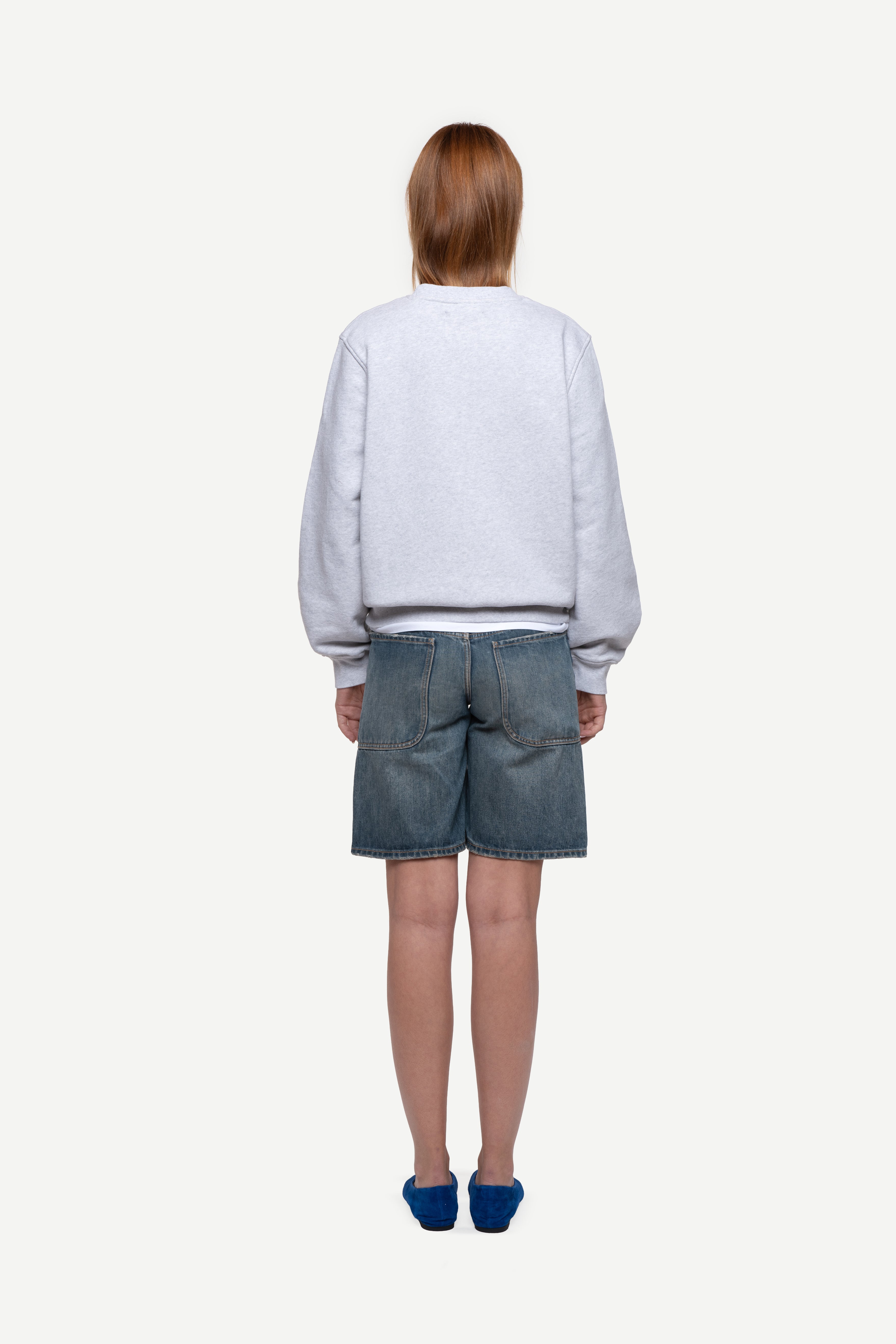 back view of woman wearing a melange grey relaxed-fit sweatshirt, blue short jeans and ballet flats on a white background