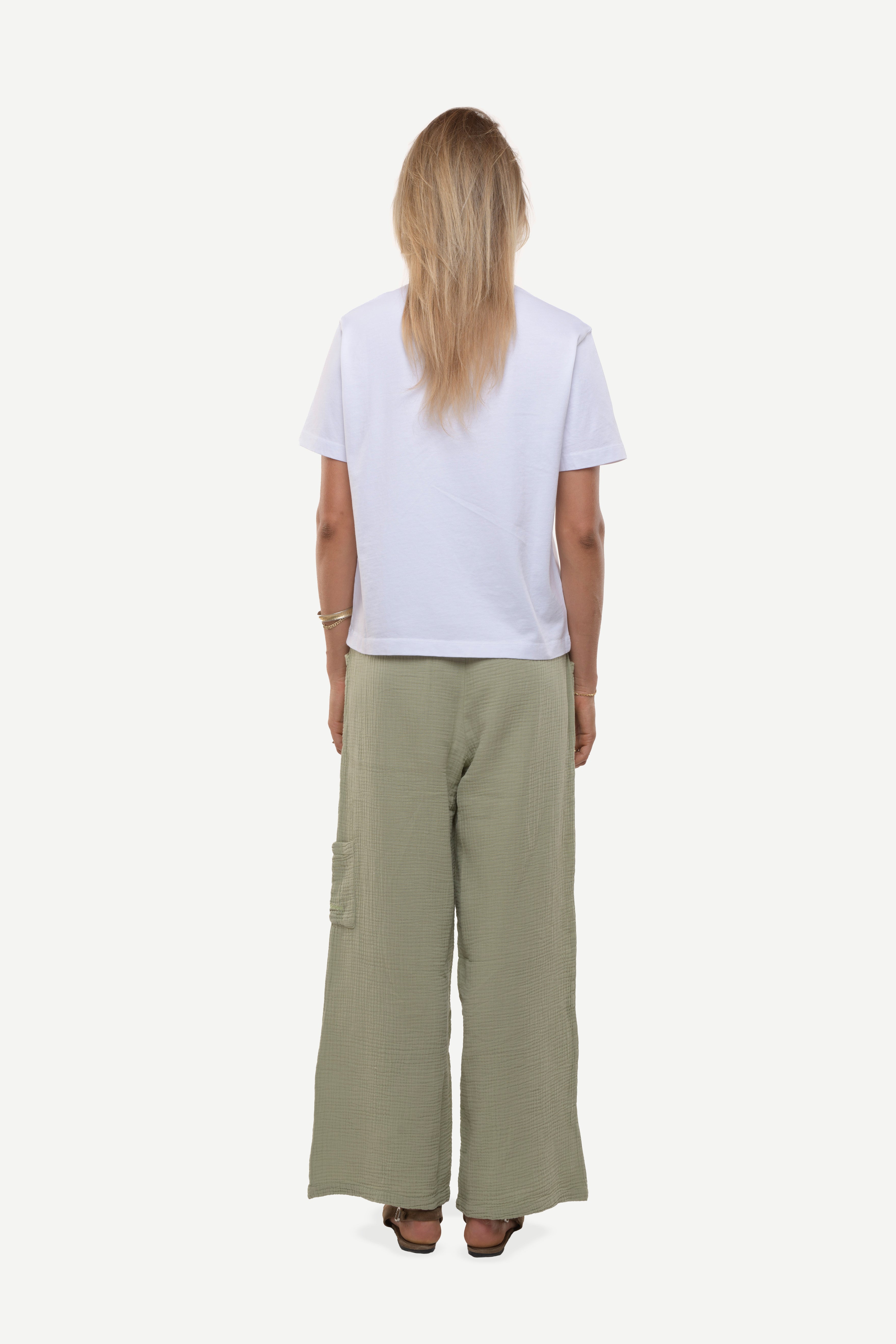 Back view of a woman wearing a white t-shirt and cotton green pants on a white background