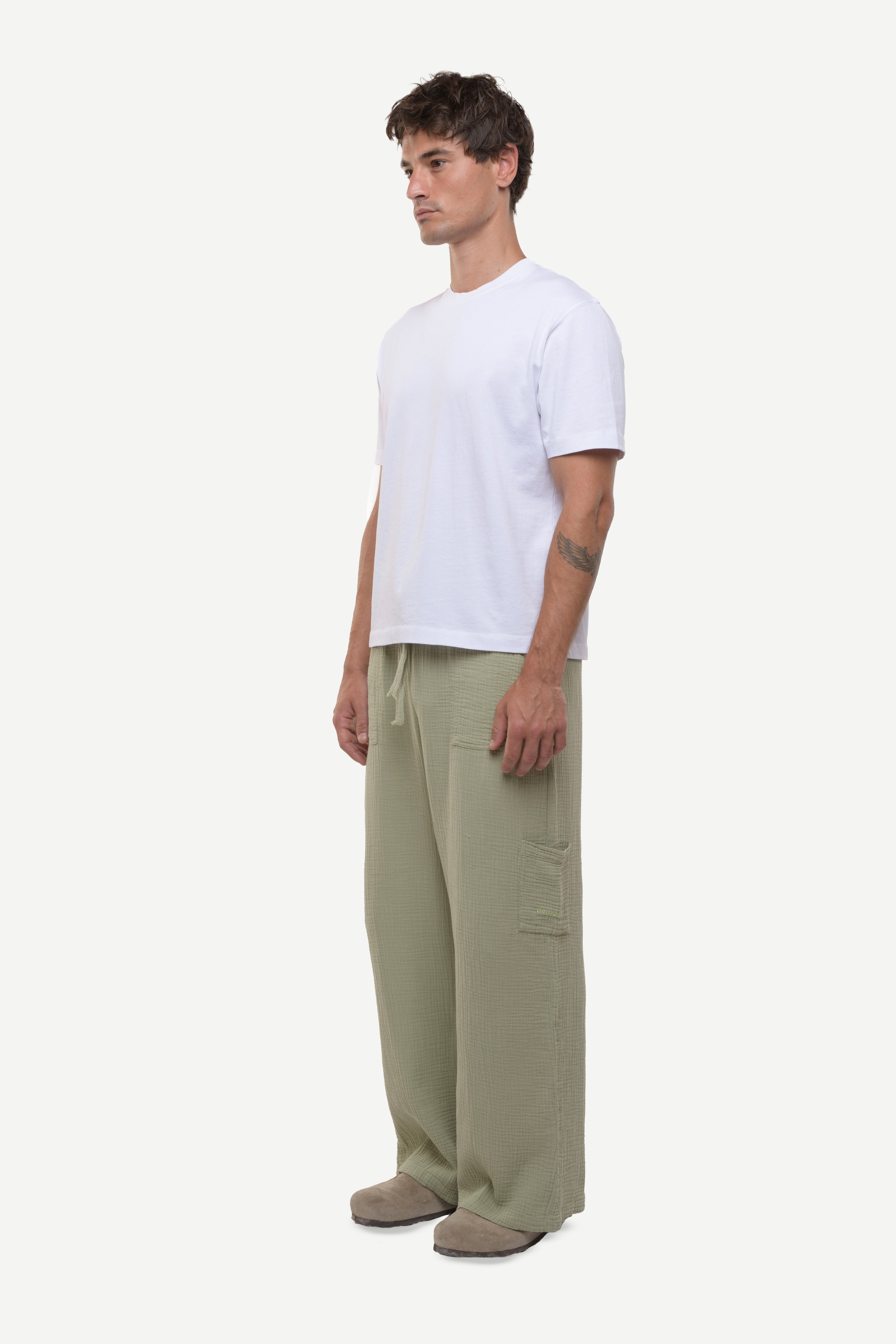 Side view of a man wearing a white t-shirt and cotton green pants on a white background