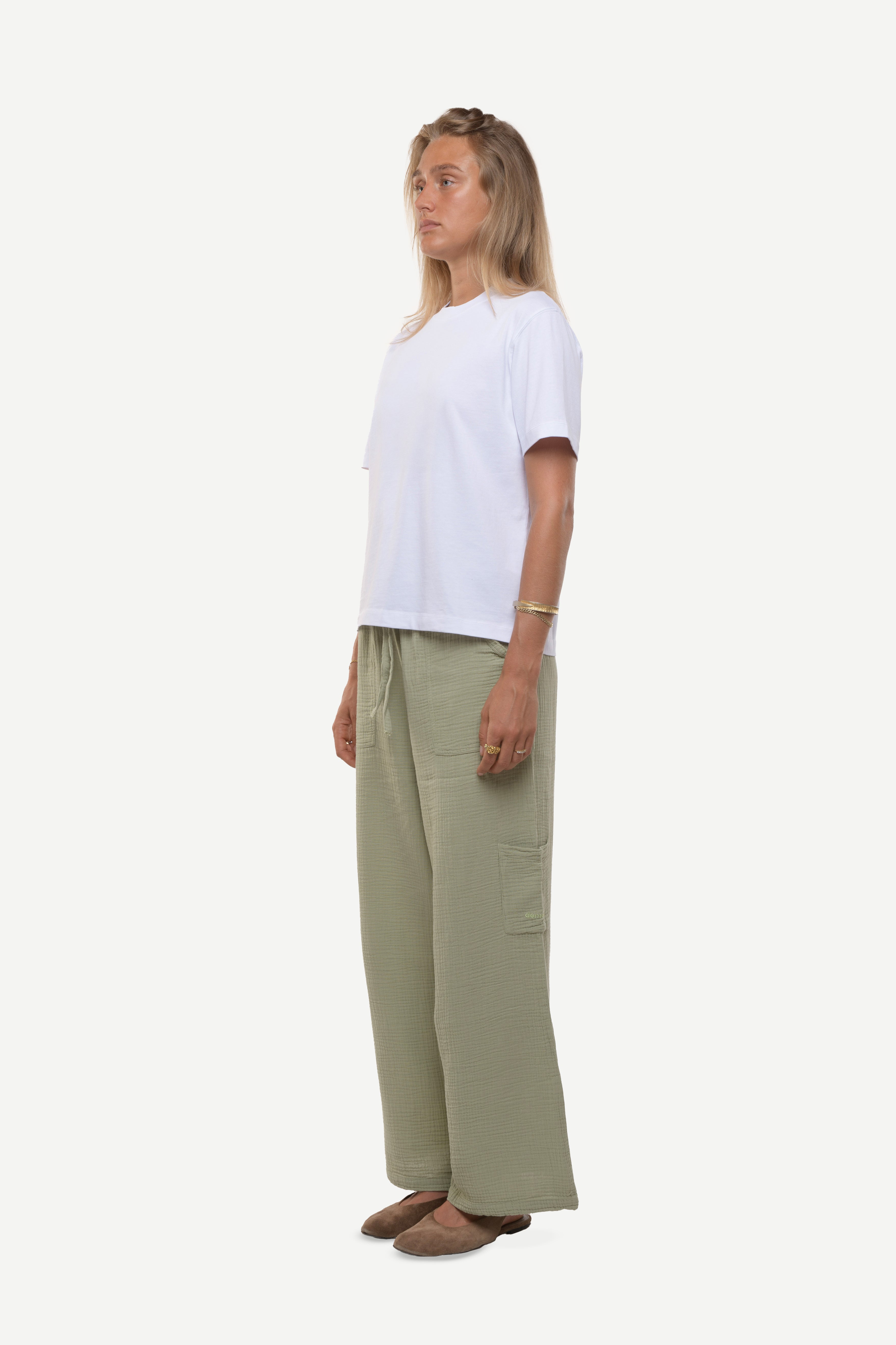 Side view of a woman wearing a white t-shirt and cotton green pants on a white background