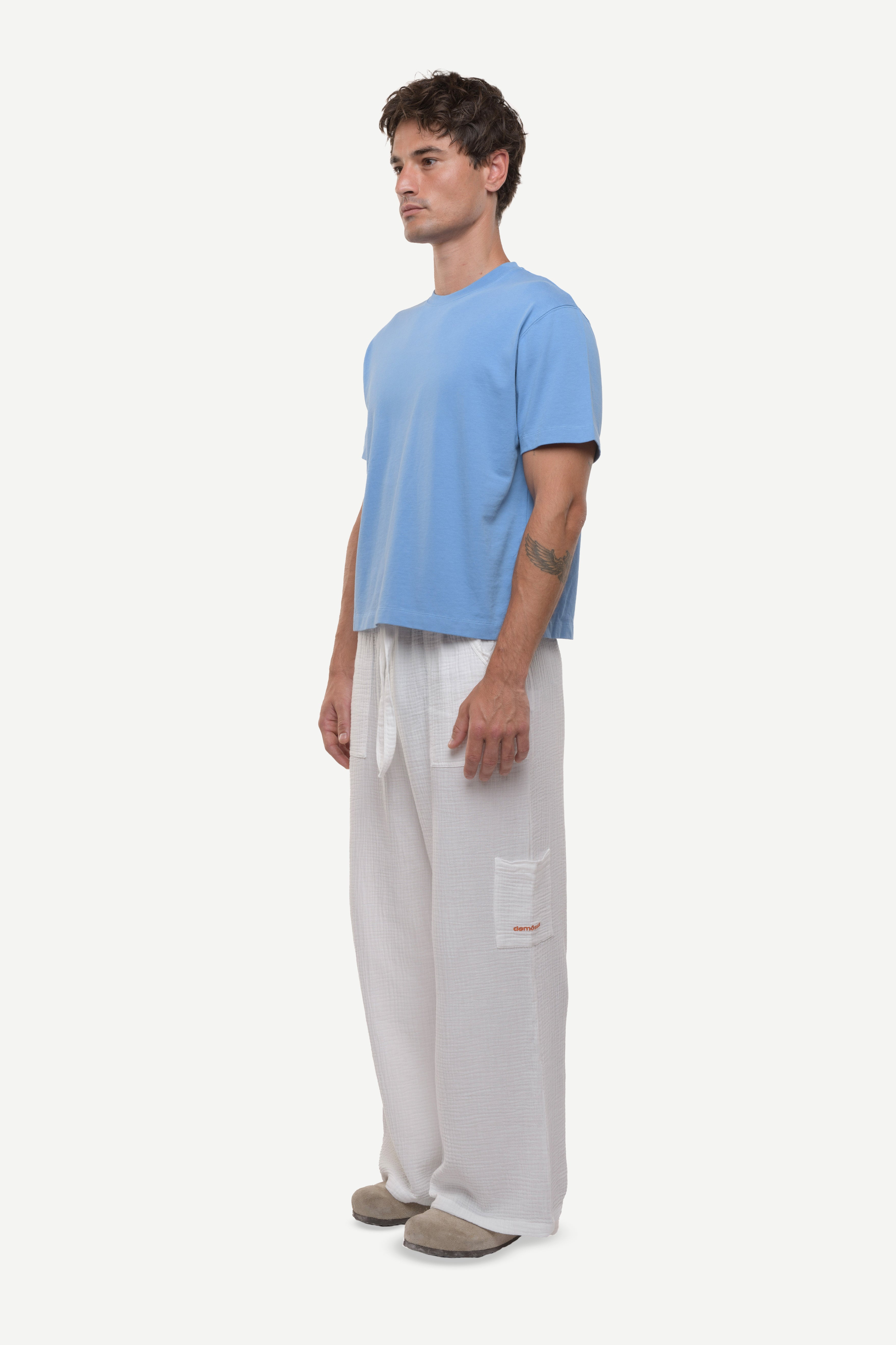 Man wearing a light blue cotton t-shirt and white cotton pants on a white background.