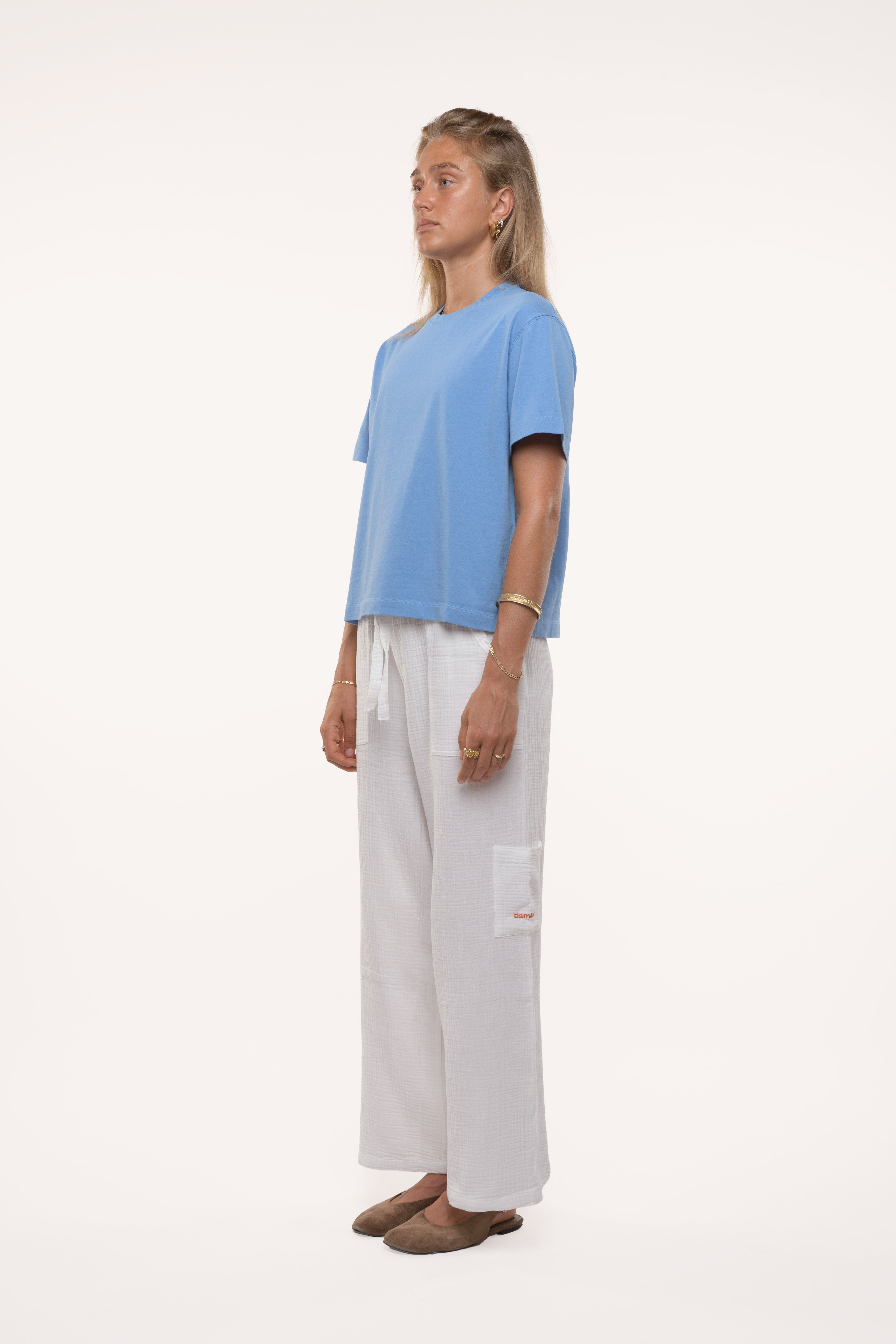 Side view of a woman wearing a light blue t-shirt and white pants on a white background