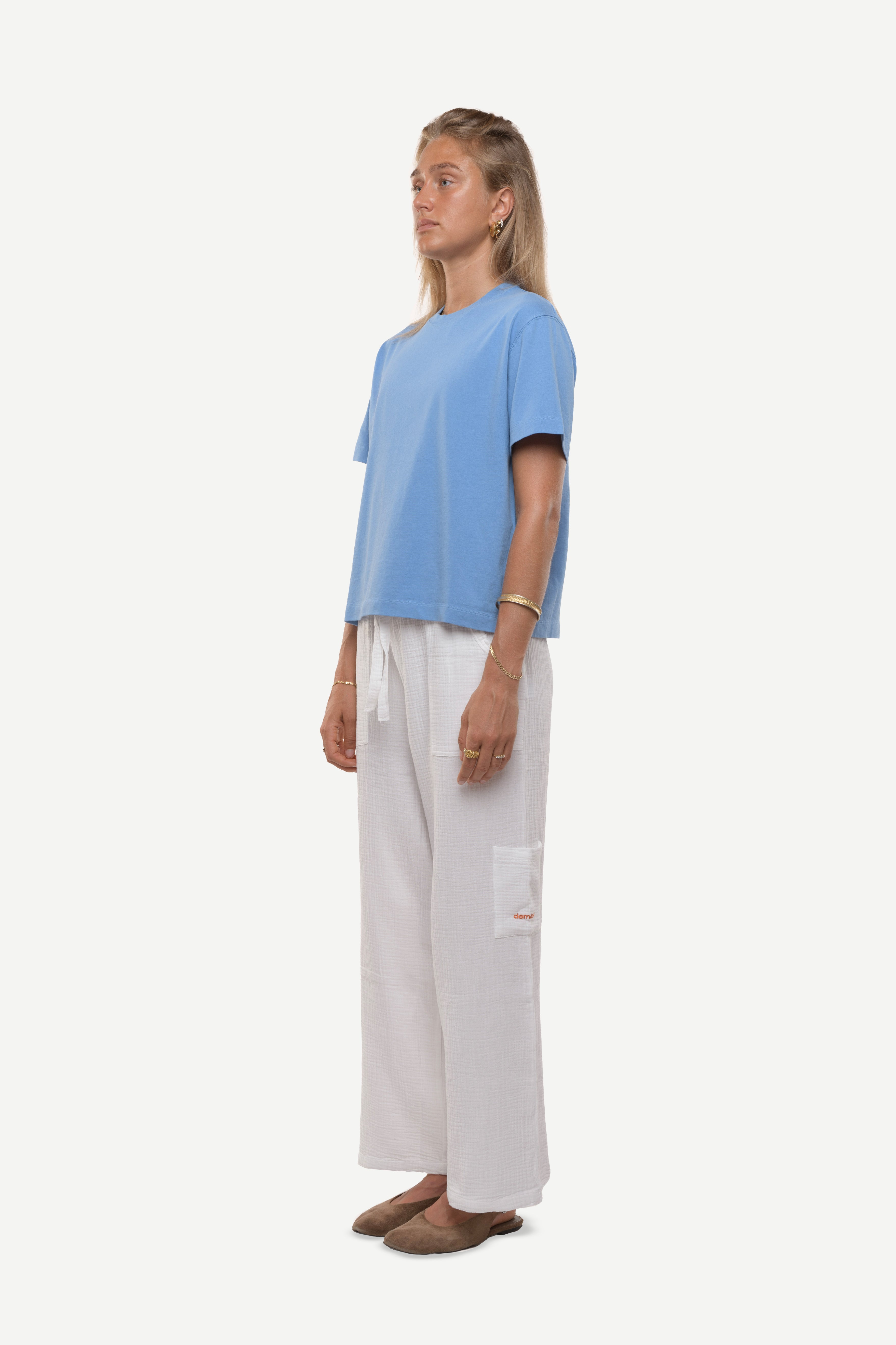 Woman wearing a light blue cotton t-shirt and white cotton pants on a white background.