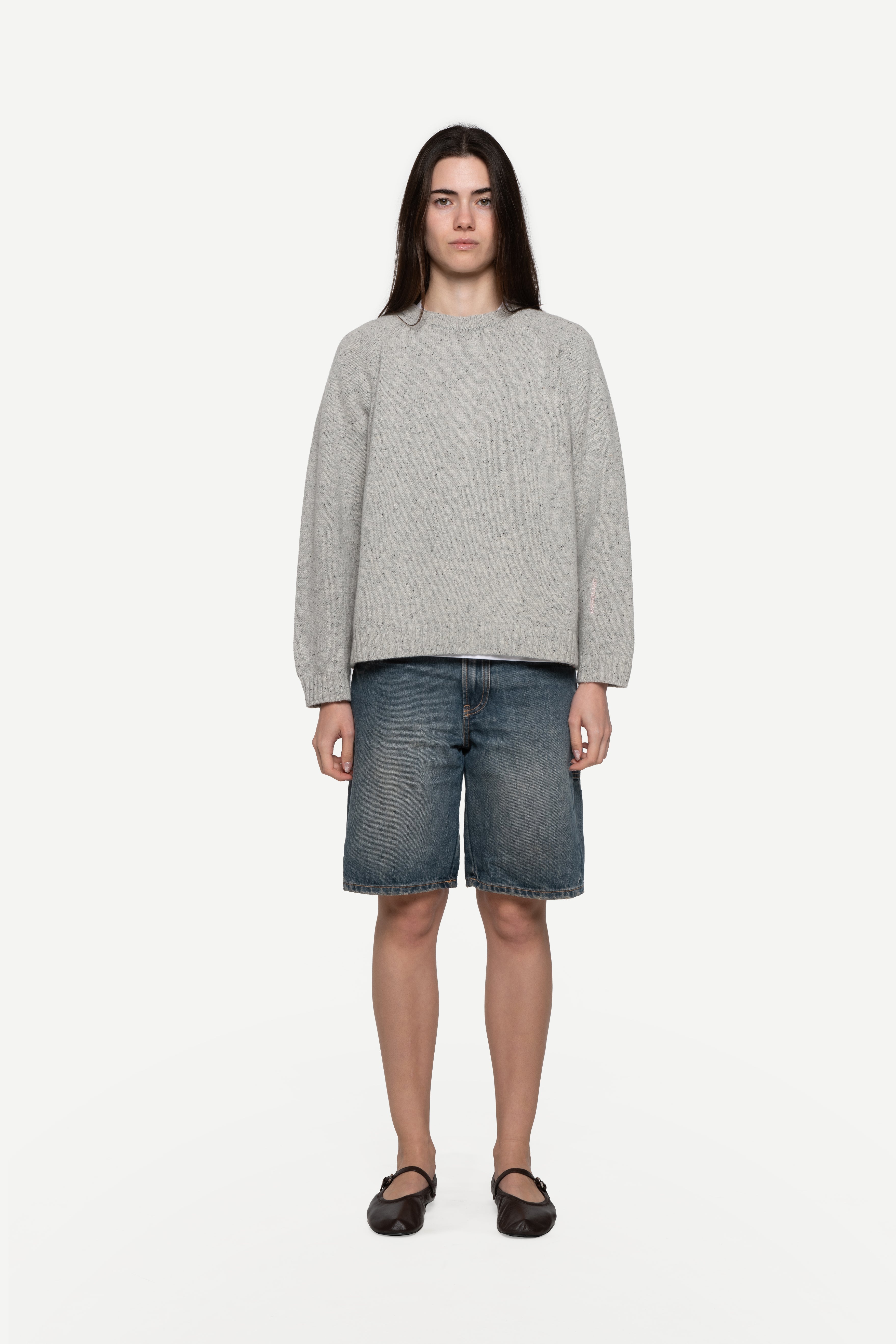 front view of woman wearing a grey sweater made from a soft blend of wool and silk with blue short jeans on a white background