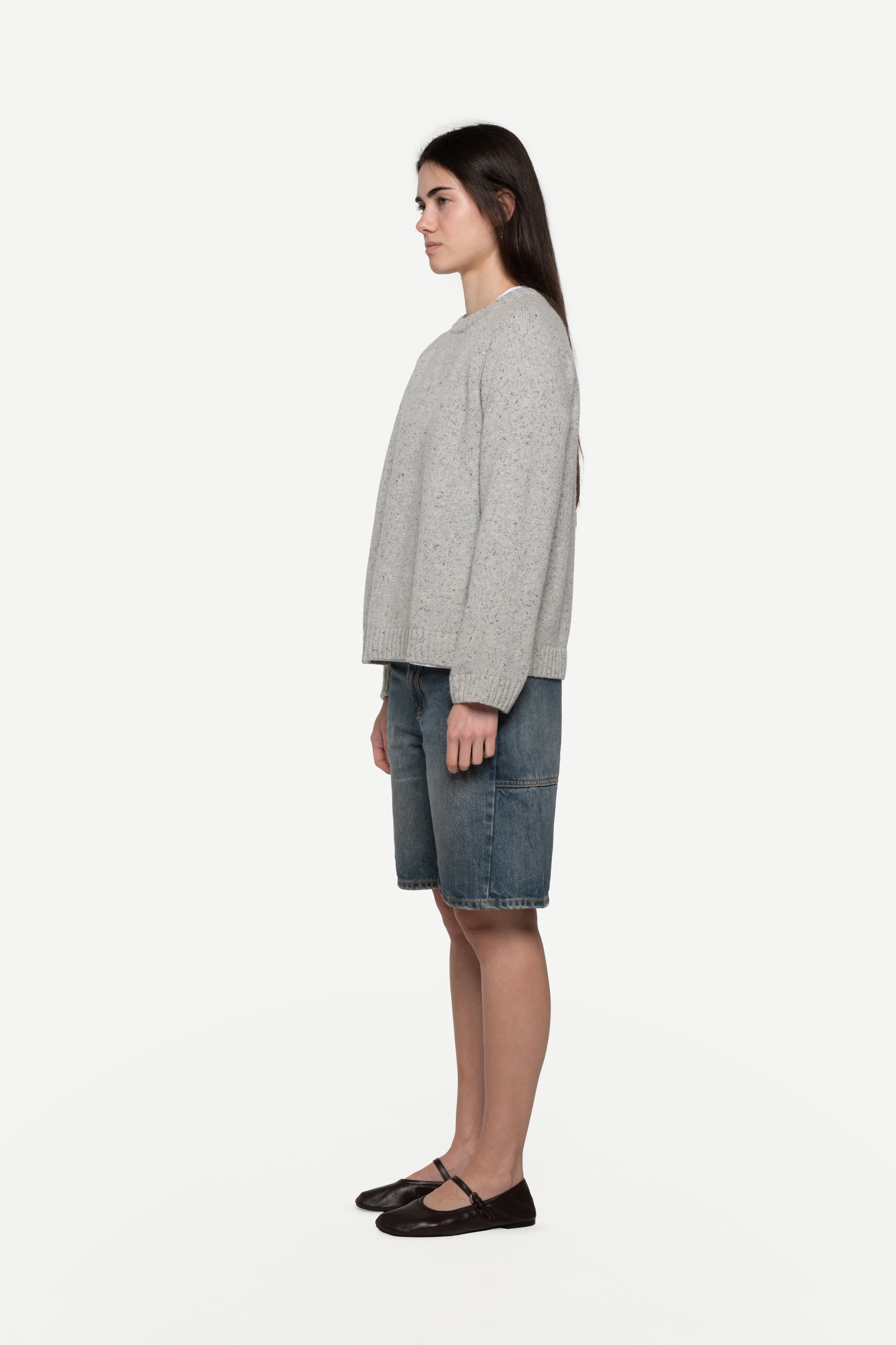 side view of woman wearing a grey sweater made from a soft blend of wool and silk with blue short jeans on a white background