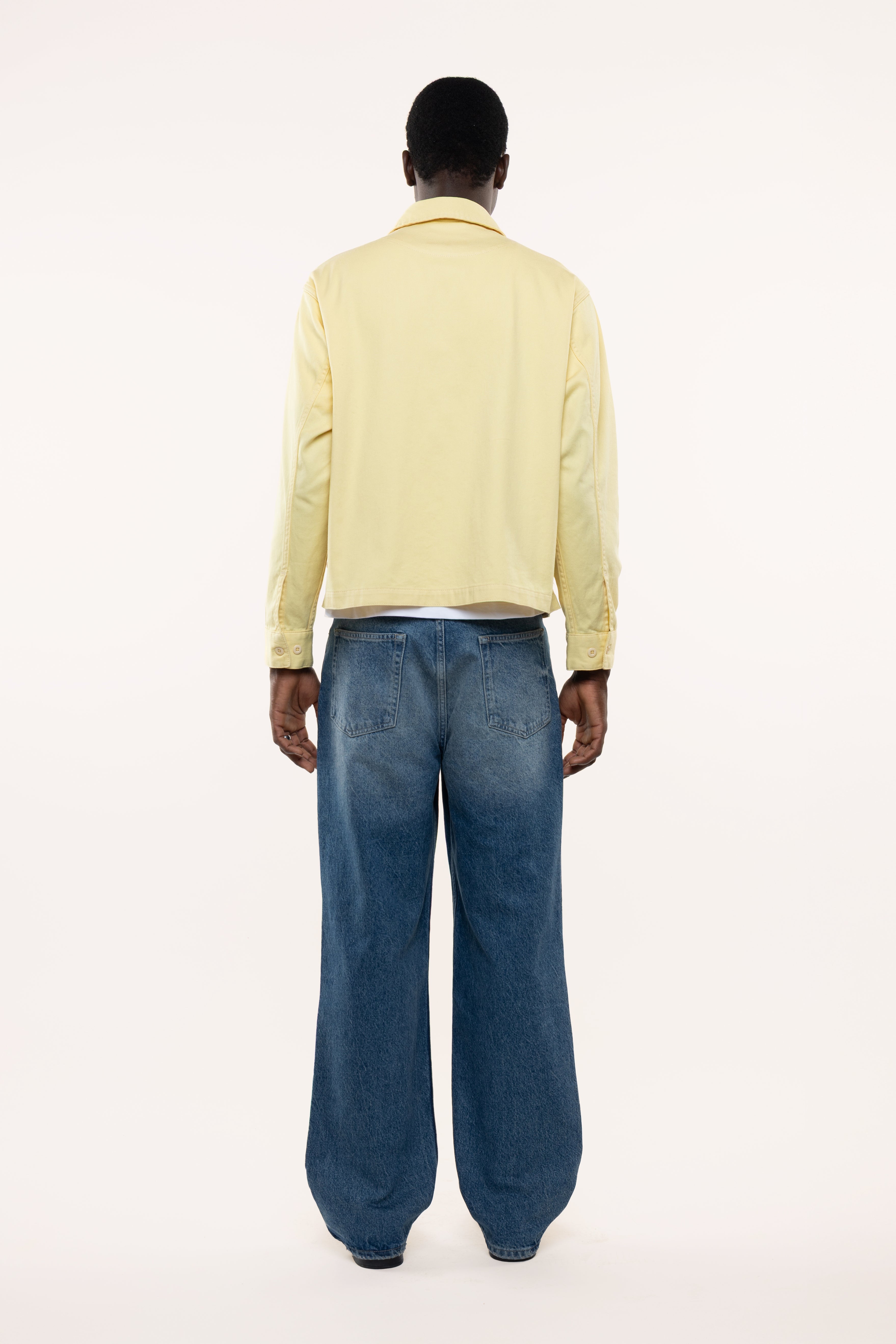 Back view of a man wearing a light yellow shirt and blue jeans on a white background