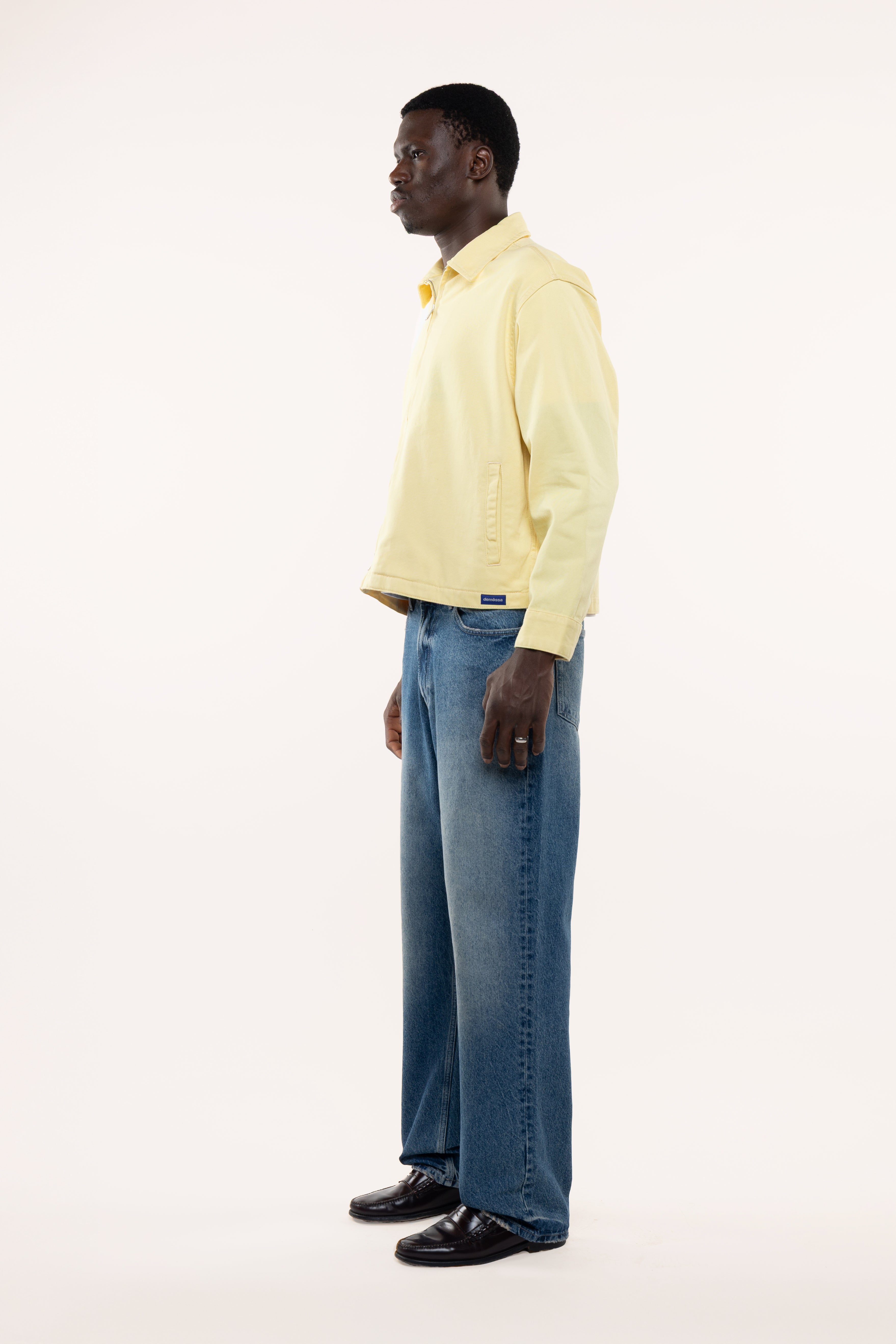 Side view of a man wearing a light yellow shirt and blue jeans on a white background