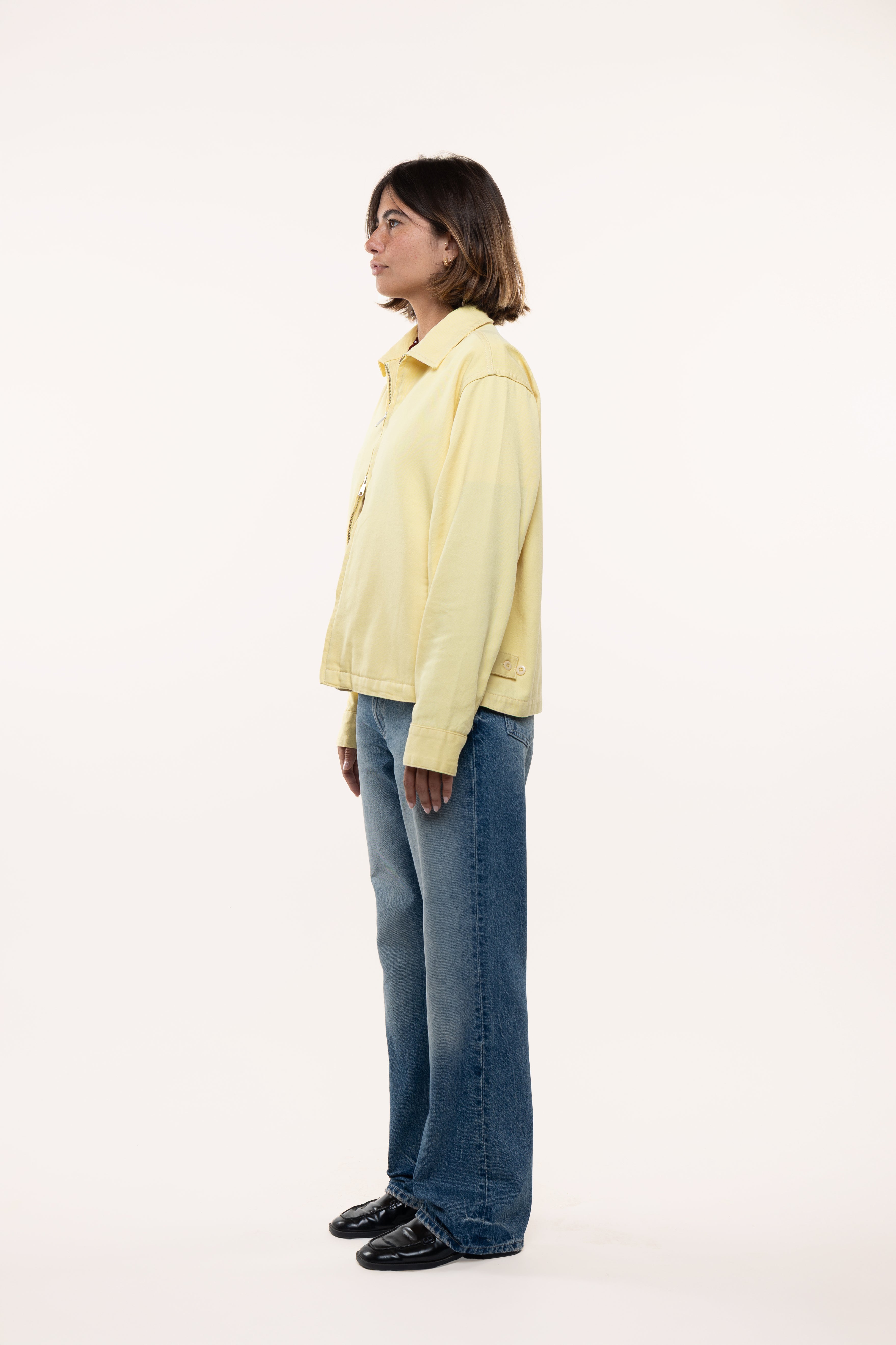 Side view of a girl wearing a light yellow jacket and blue jeans on a white background