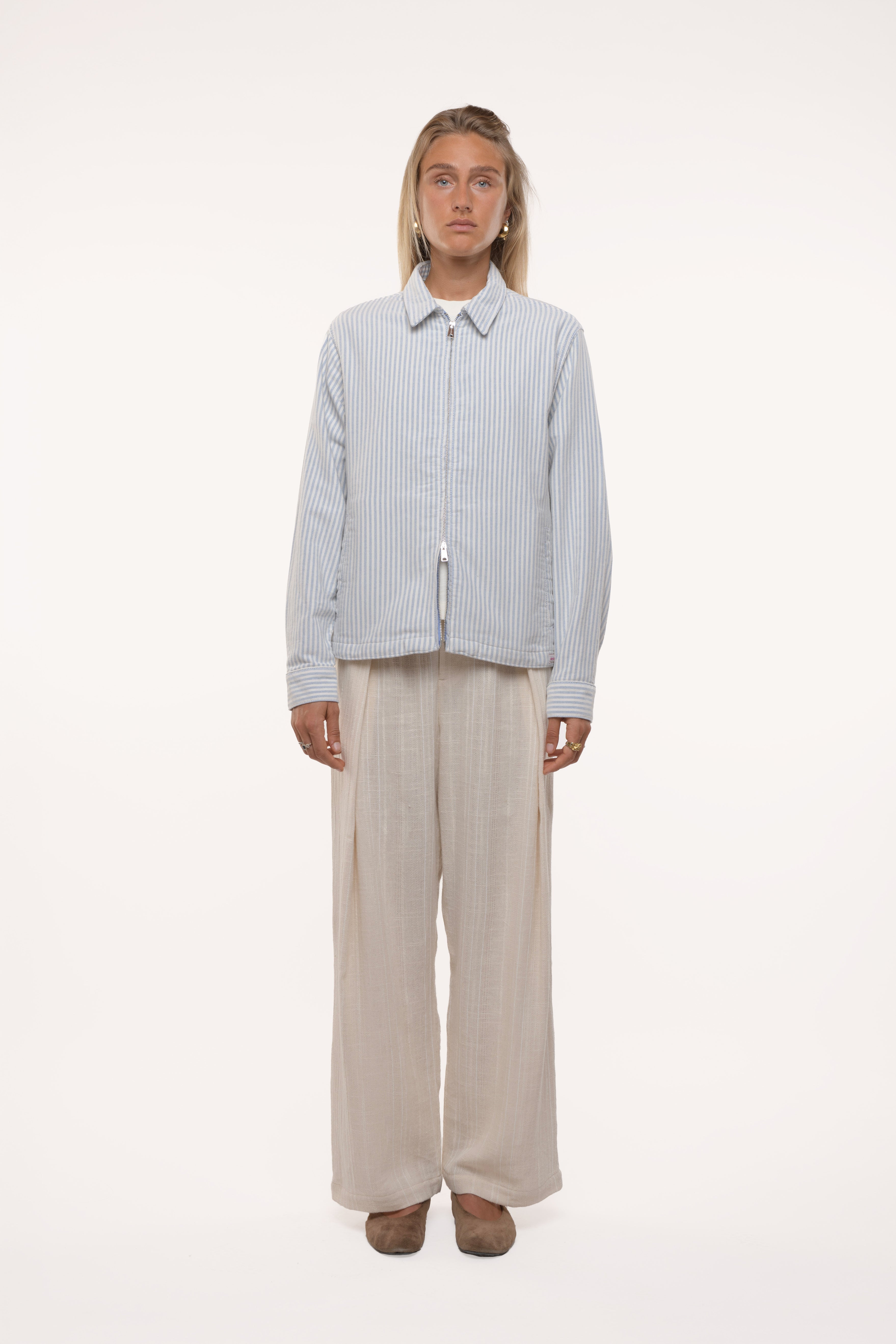 Woman wearing a light blue striped shirt and beige pants on a white background