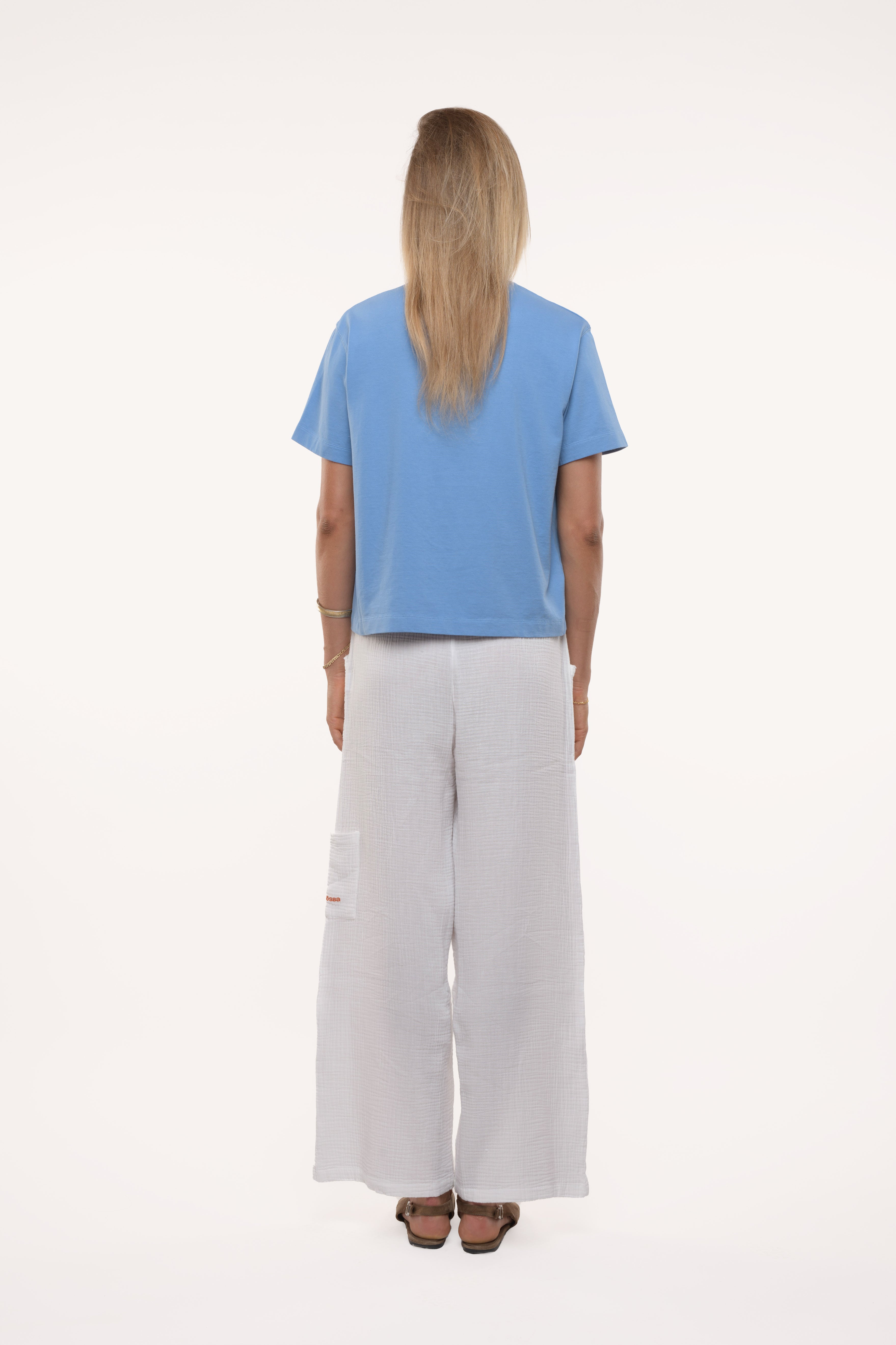 Back view of a girl wearing a blue shirt and light gray pants on a white background
