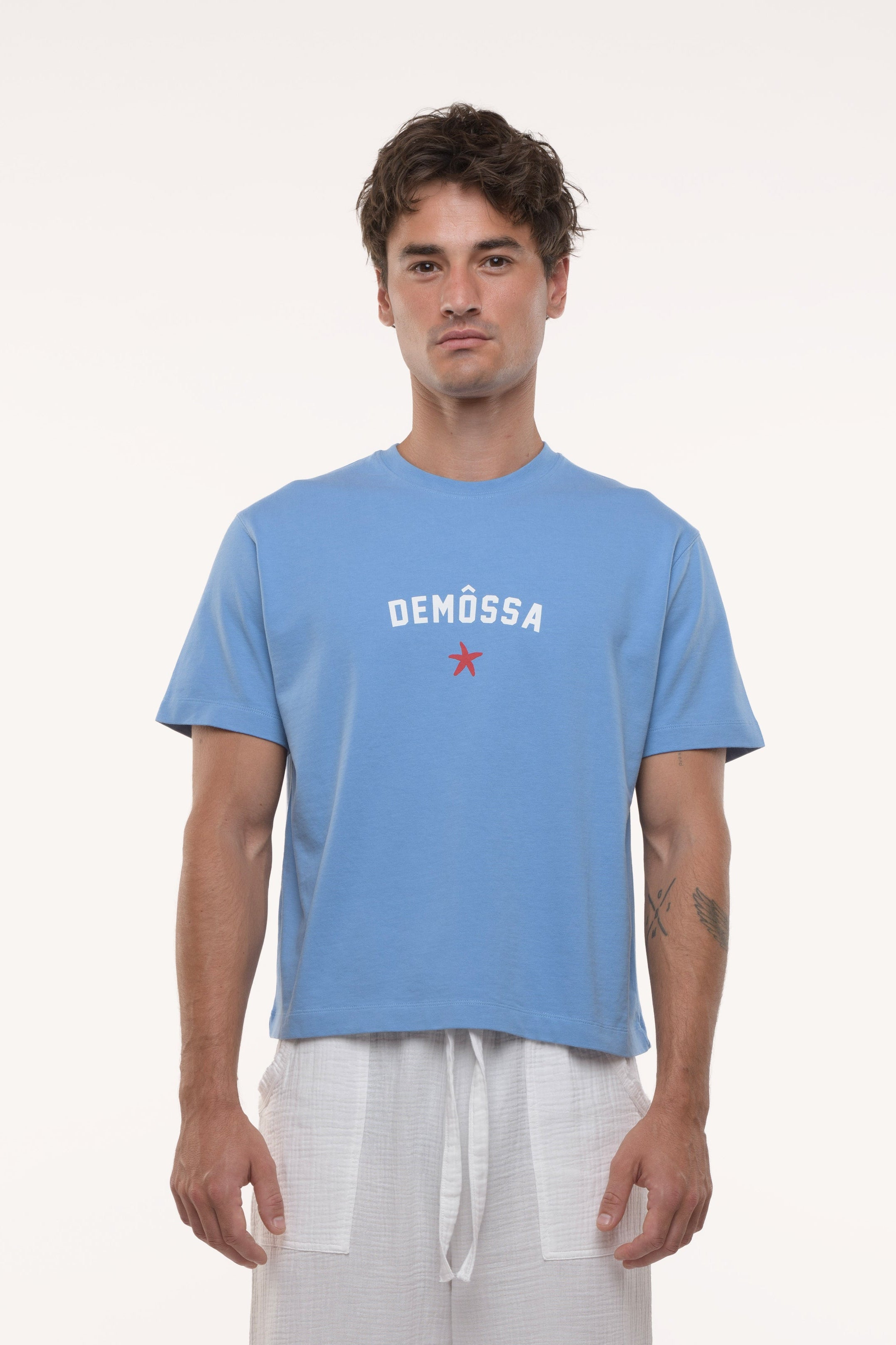 Man wearing a blue t-shirt with 'DEMOSSA' logo on a white background
