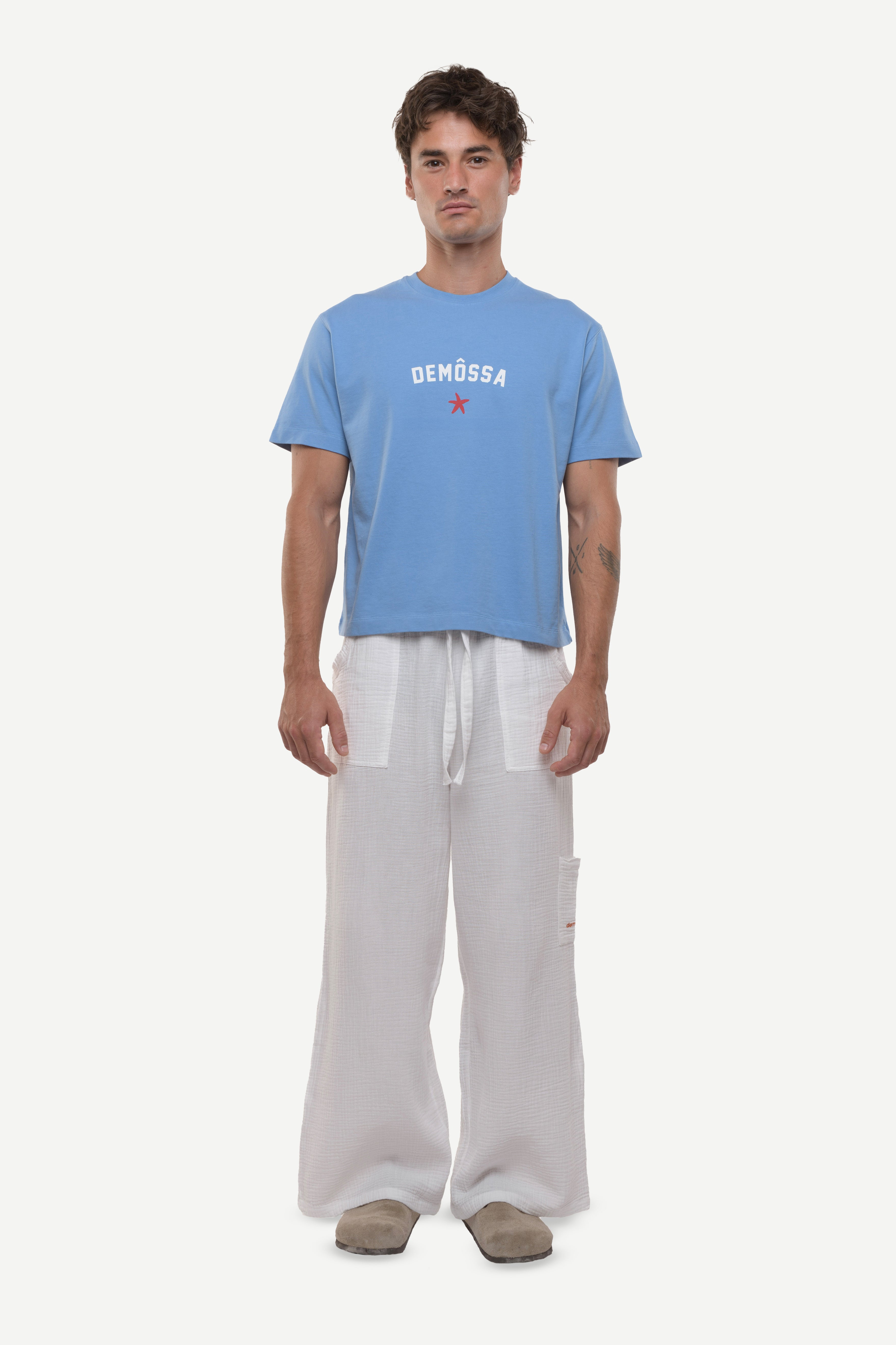 Man wearing a blue t-shirt with 'DEMOSSA' logo on a white background